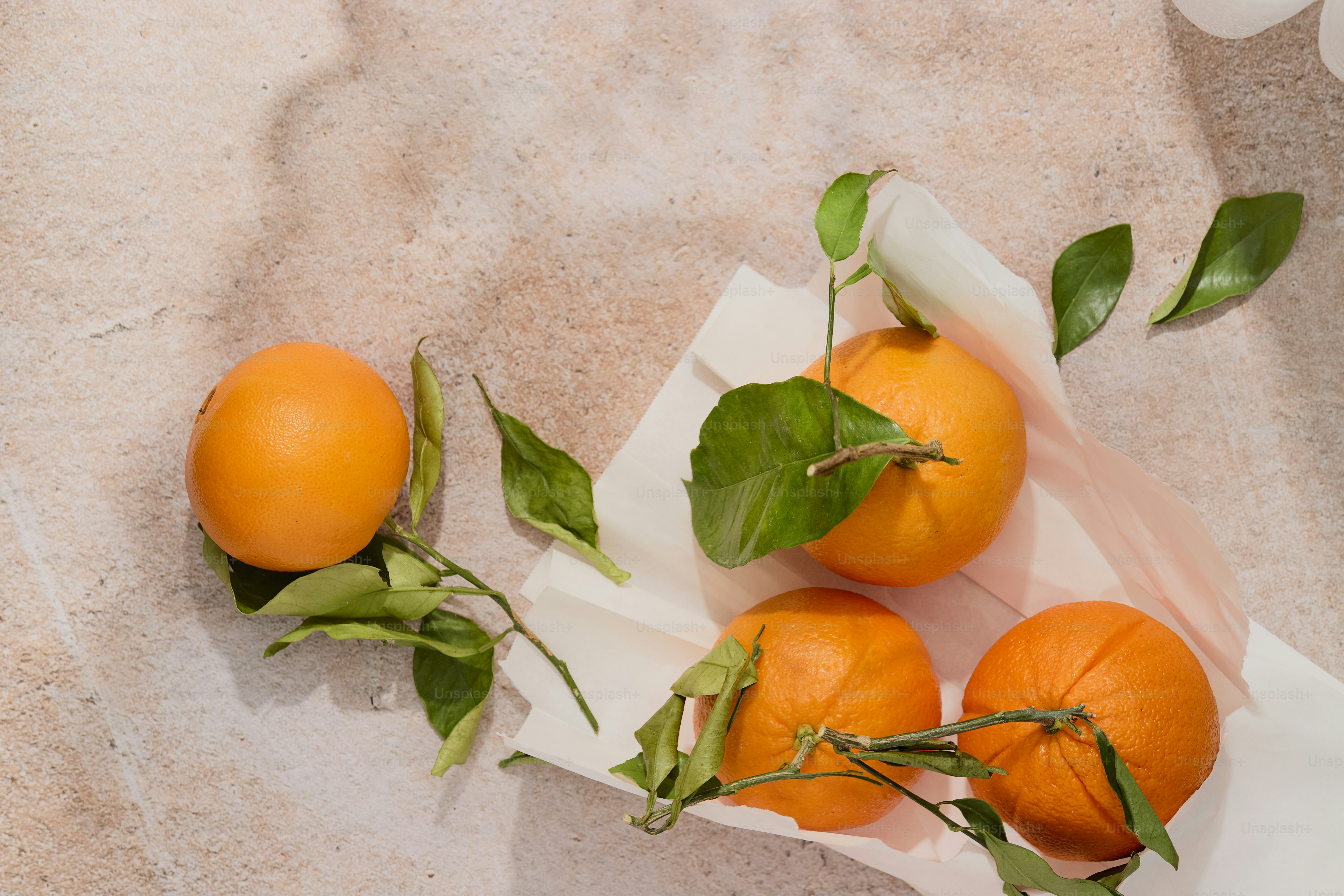 Oranges with leaves in paper bag on stone, dappled shadow.
