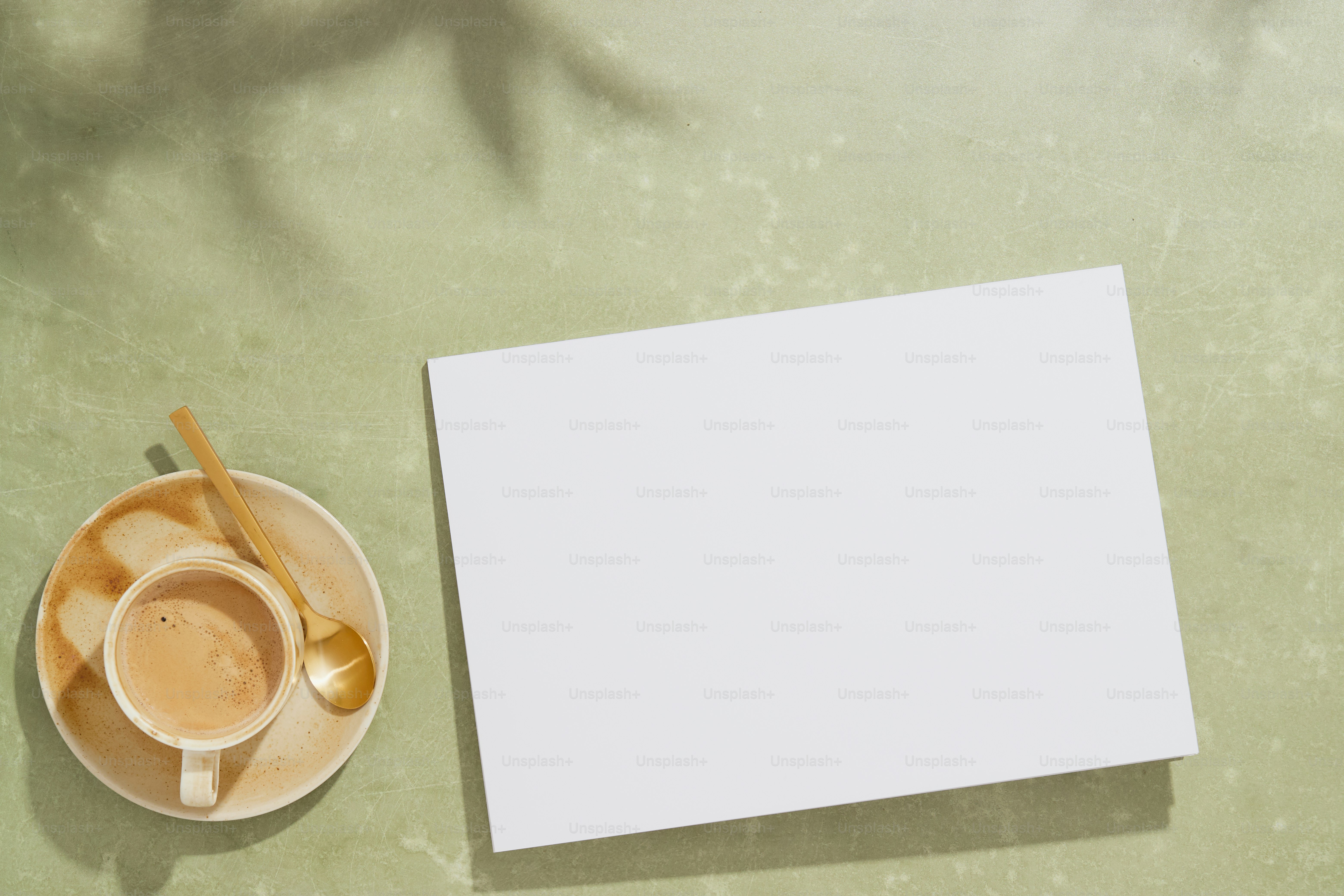Coffee cup, spoon, blank page on sunlit green surface