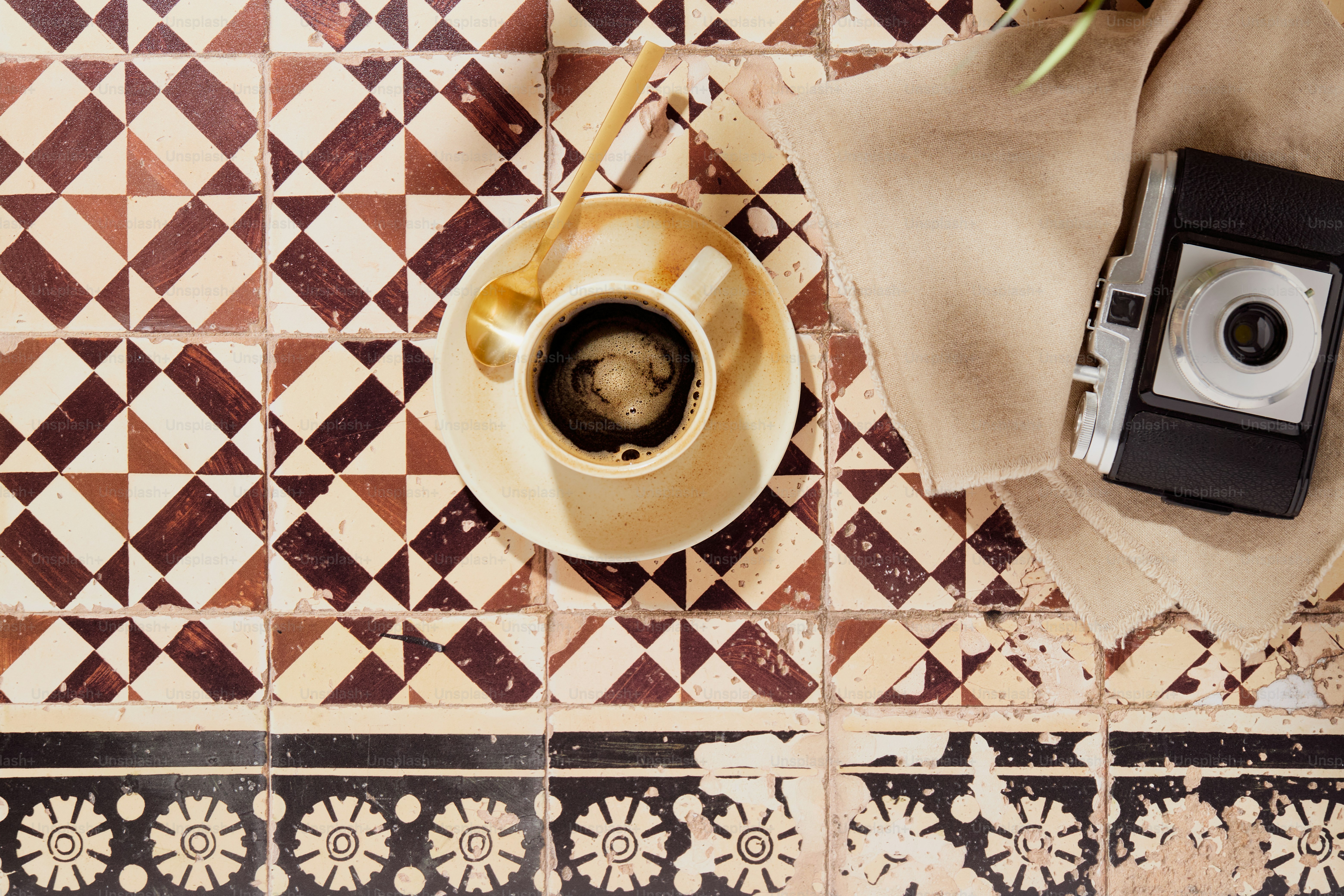 Coffee cup, vintage camera on patterned tiles, bright sun.