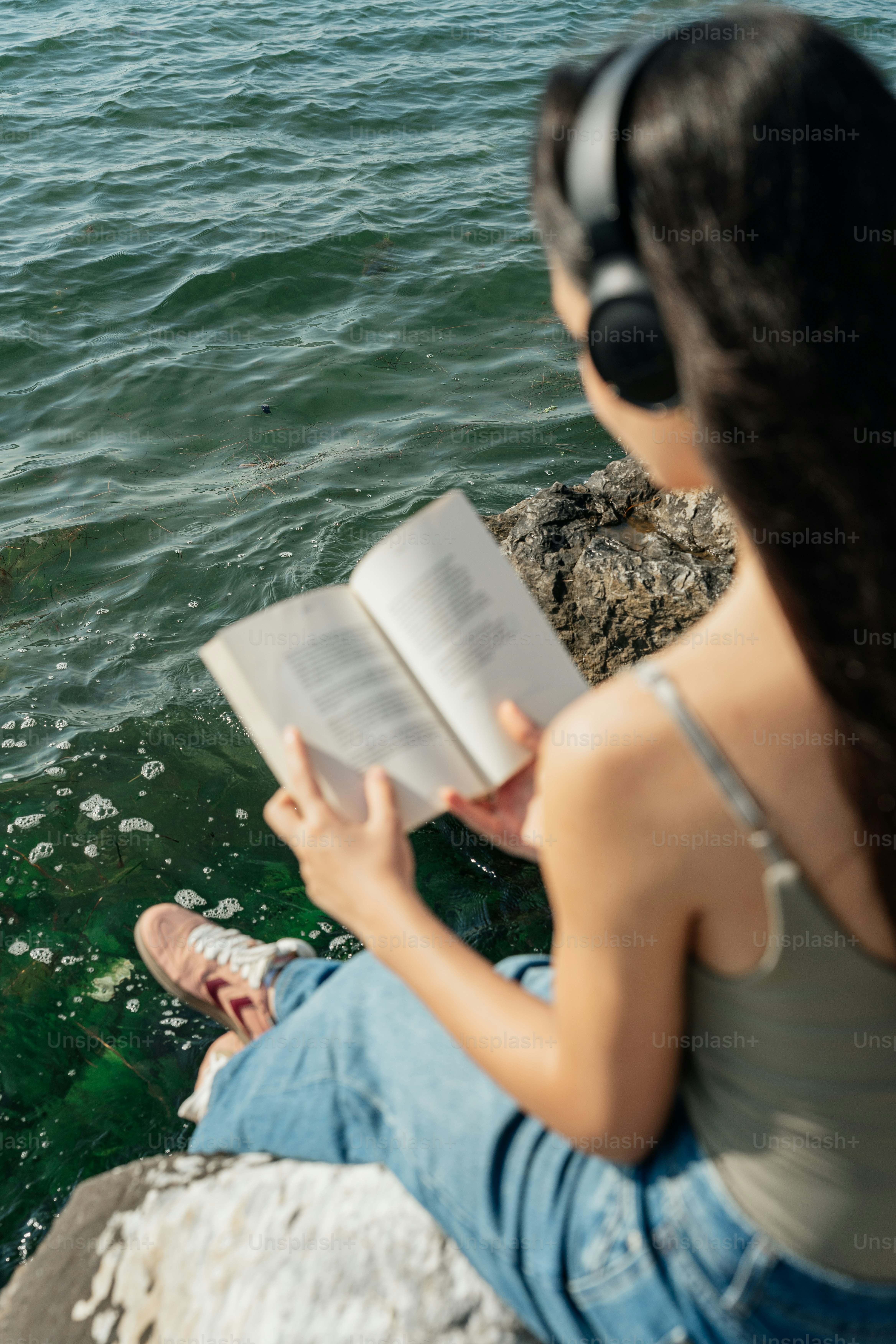 Woman reading book, wearing headphones by the water