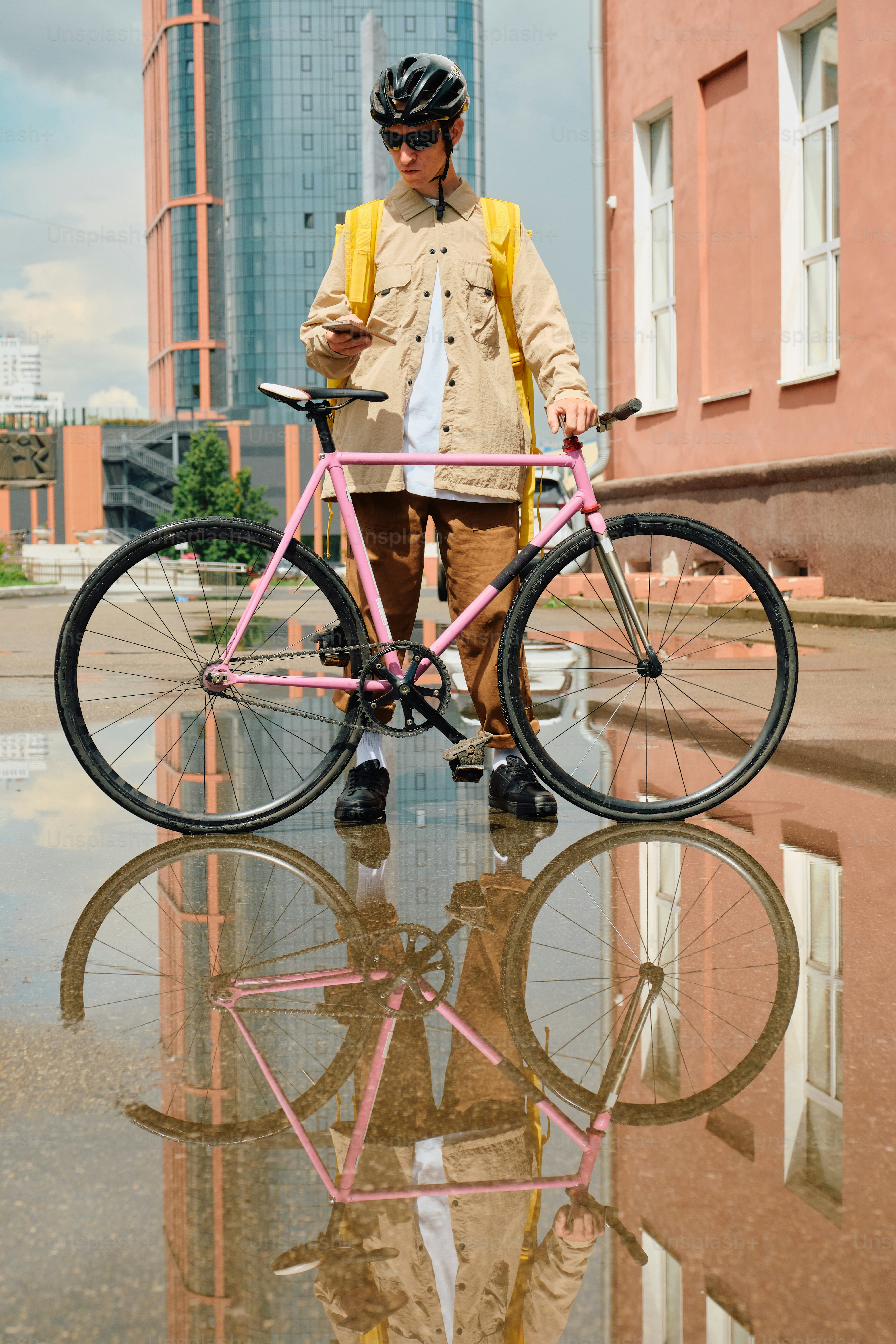 Delivery rider checking phone, bicycle reflected in puddle