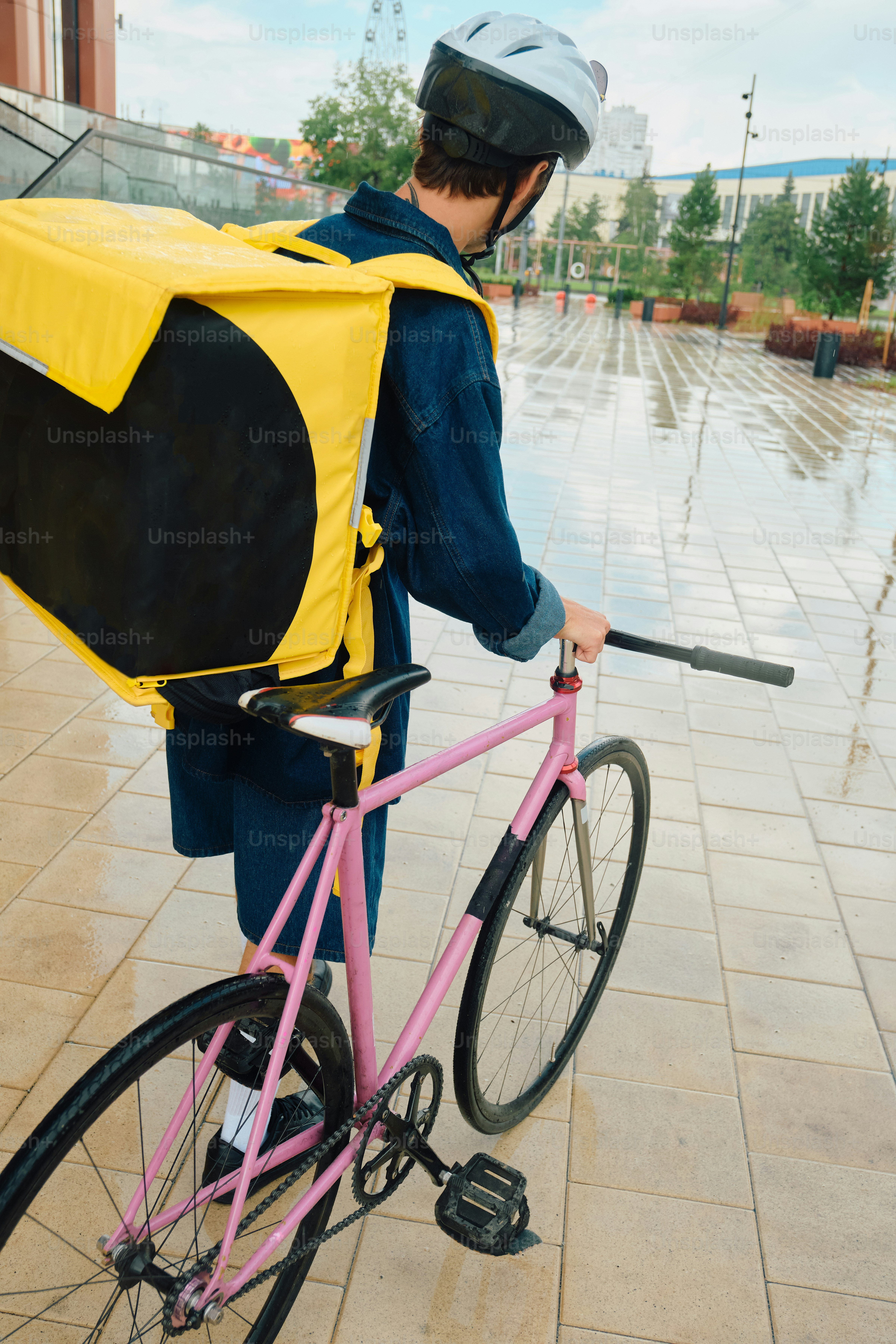 Delivery rider with bicycle on wet city street
