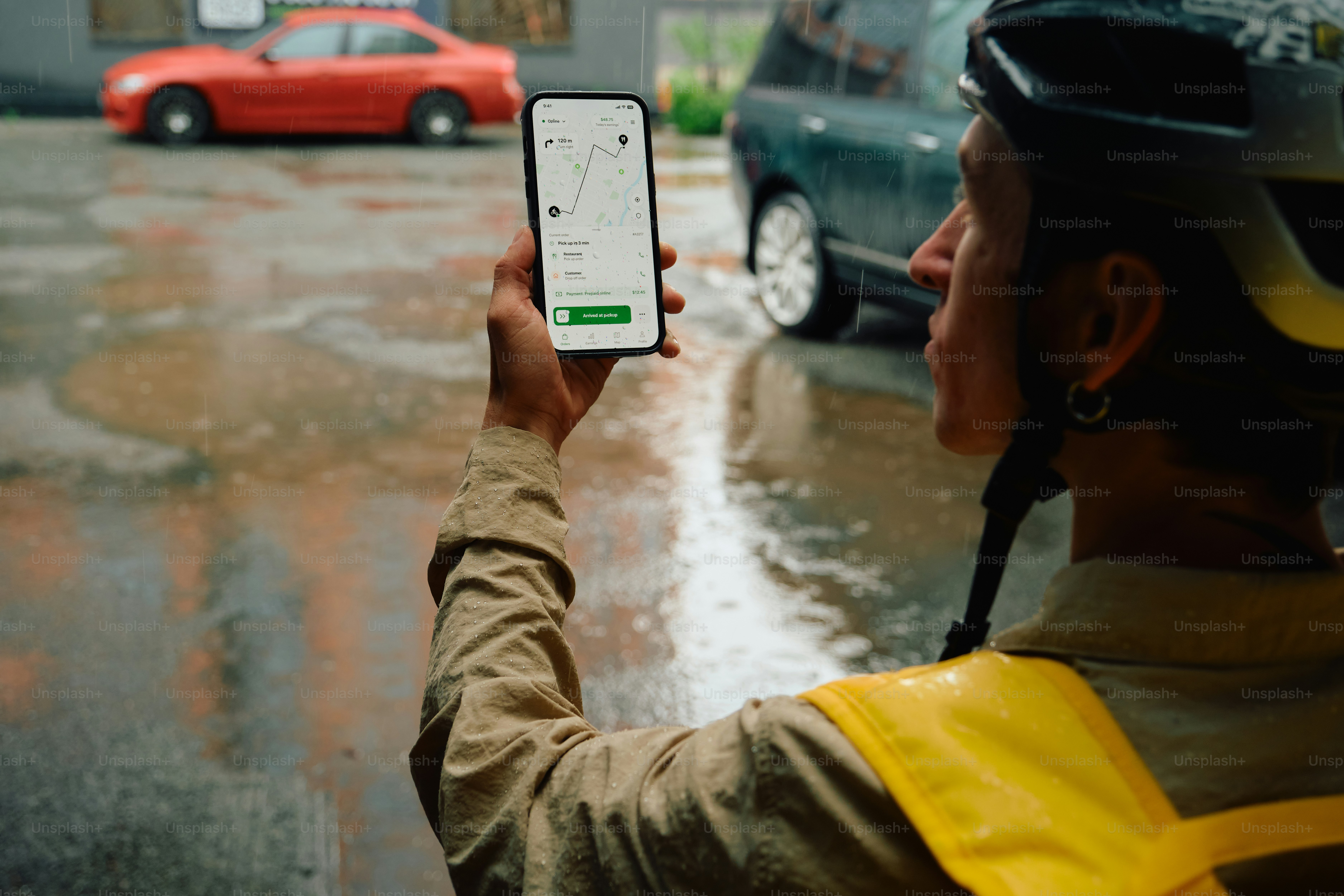 Delivery rider checking delivery app on wet city street