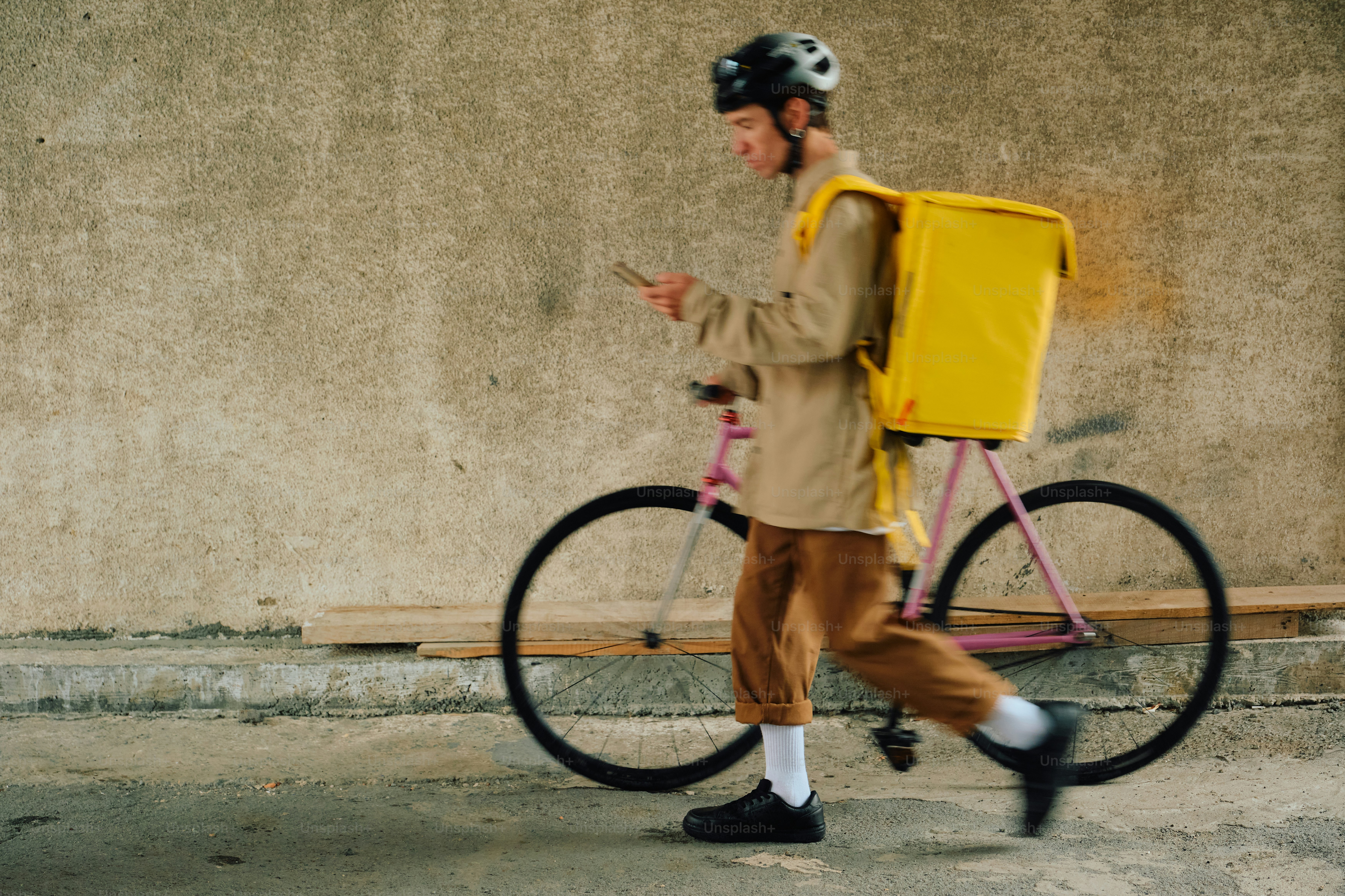Delivery rider checking phone while walking with bicycle