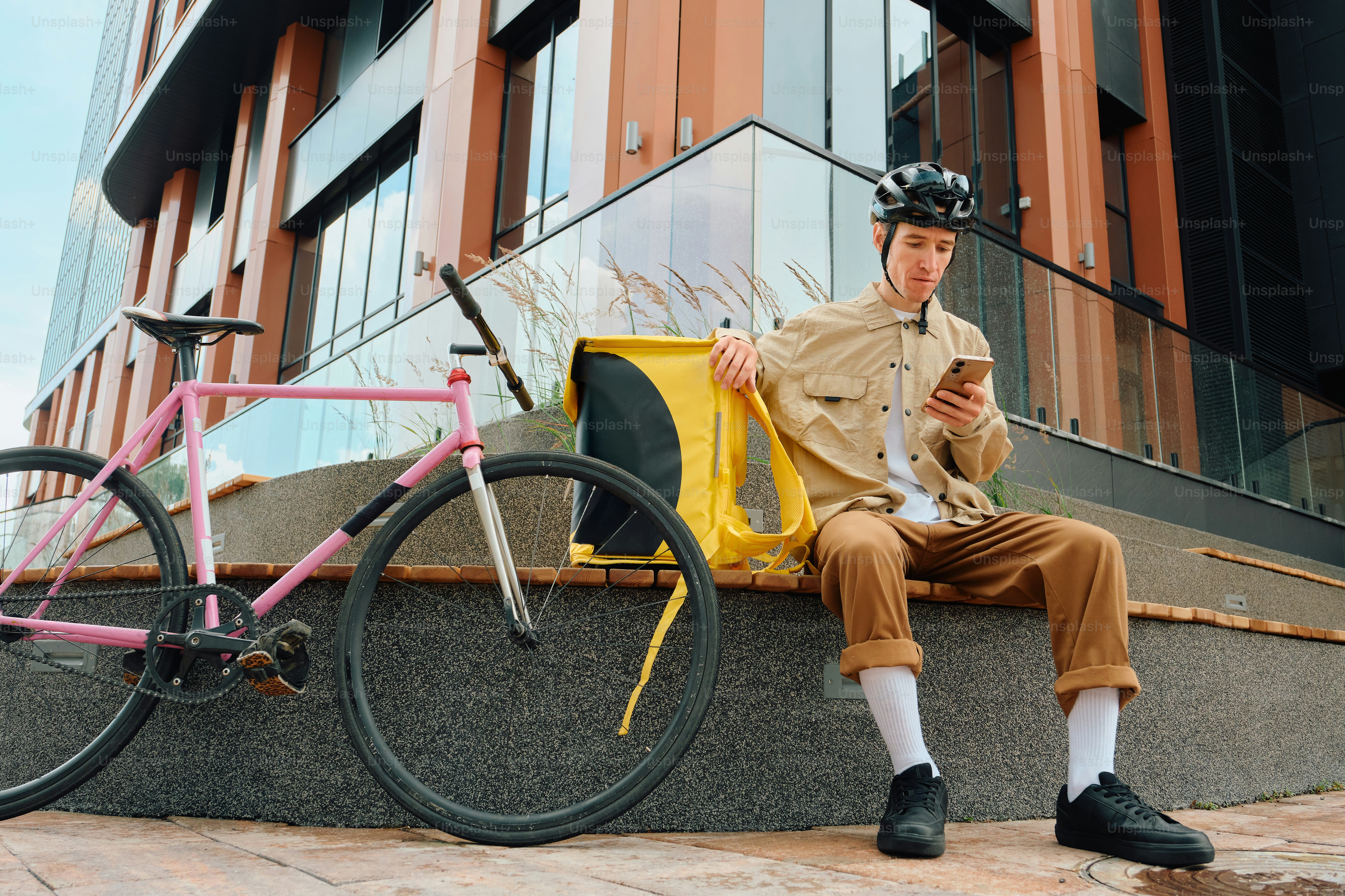 Delivery rider checking phone with bicycle and yellow bag