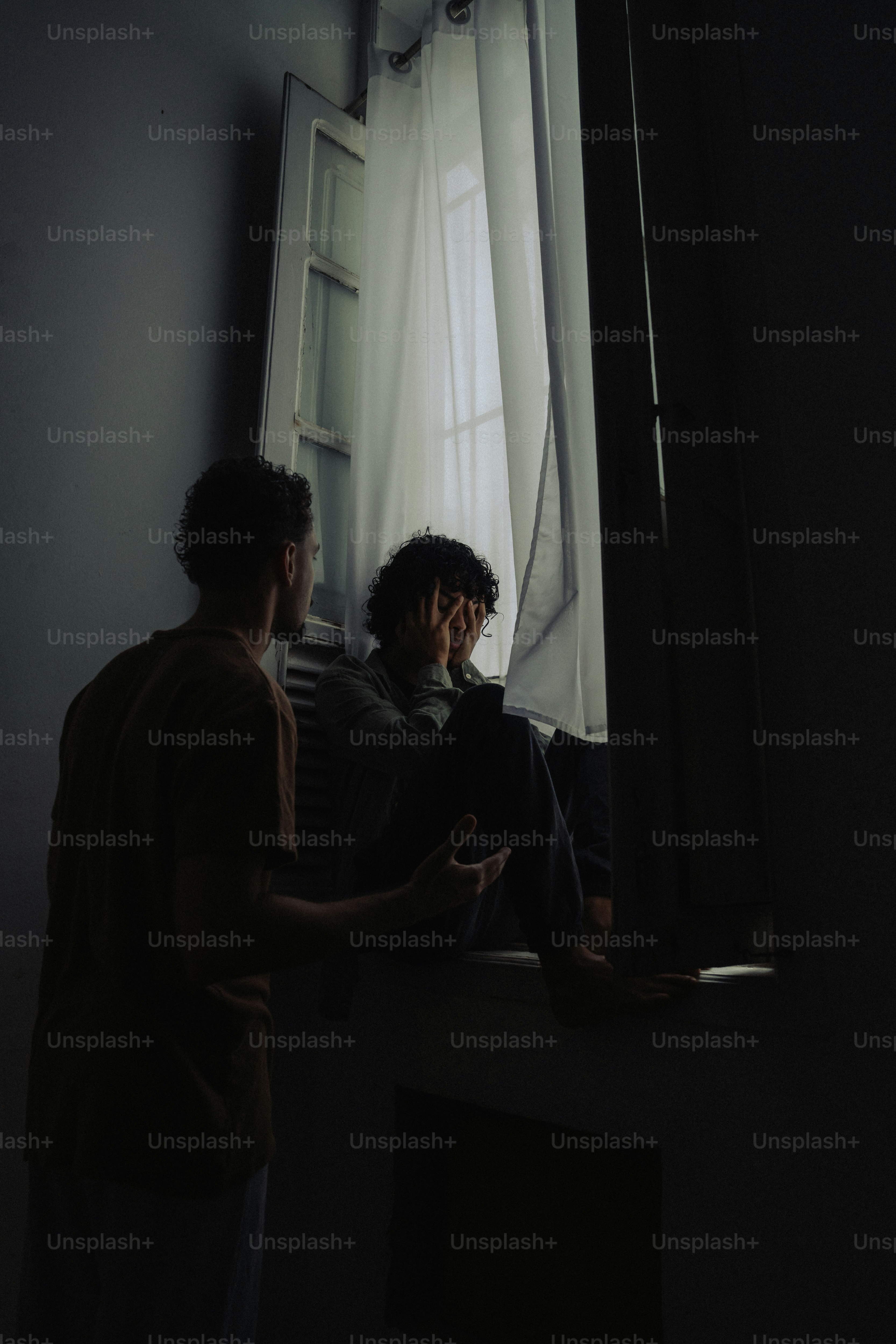 Man comforting distressed person sitting by window