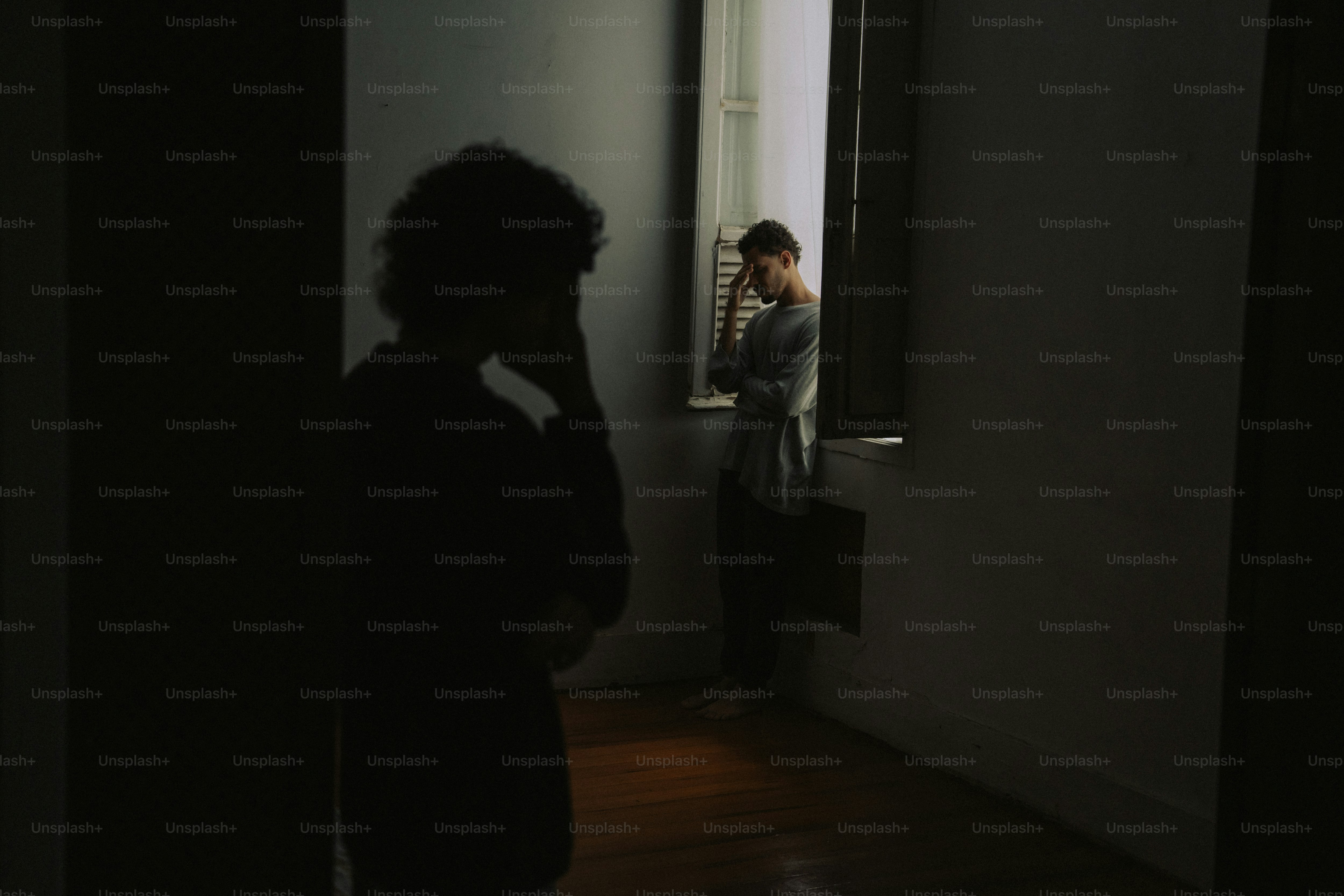 Distressed person by window, another in dark foreground