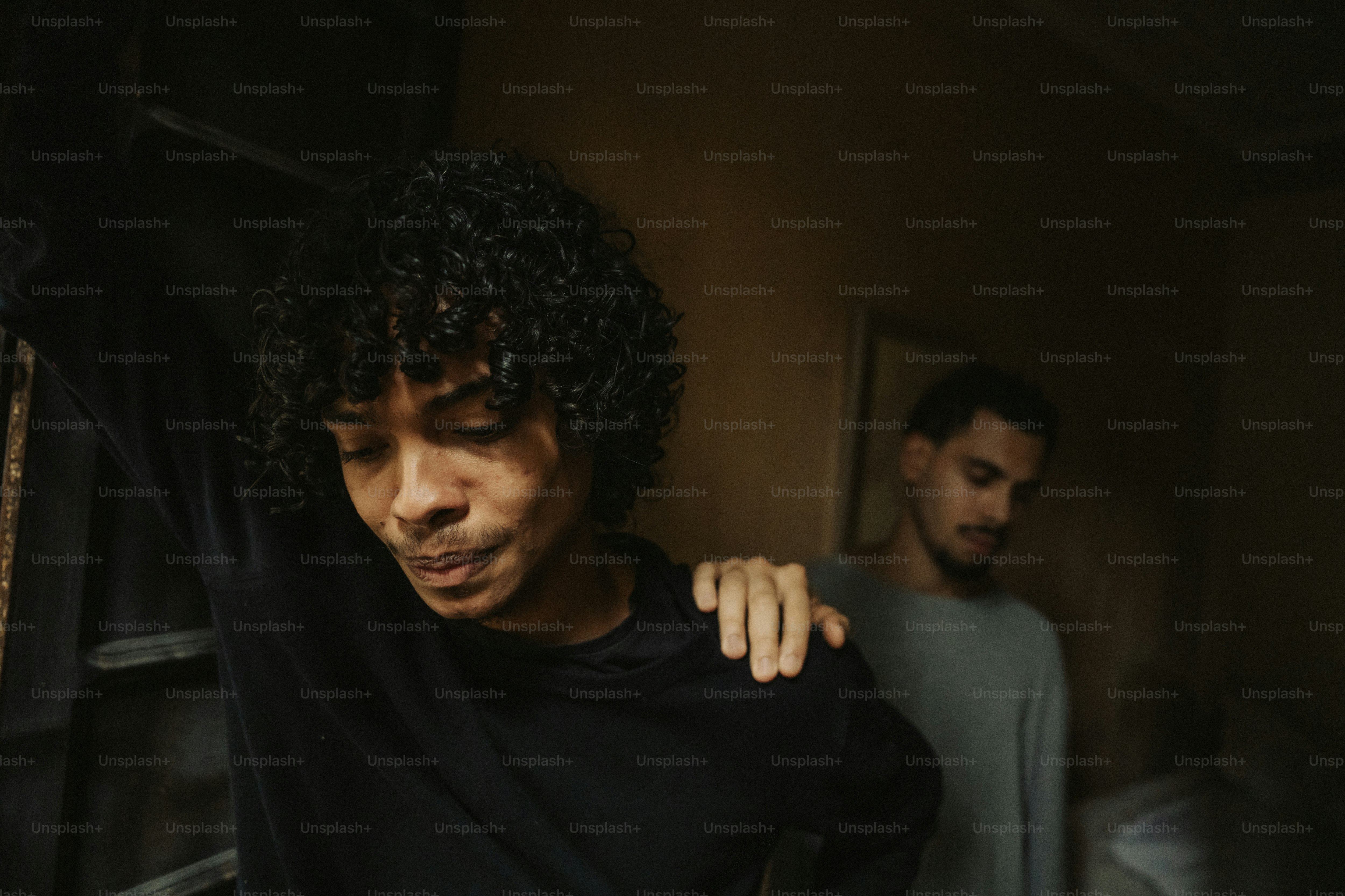 Two men in dark room, hand on shoulder