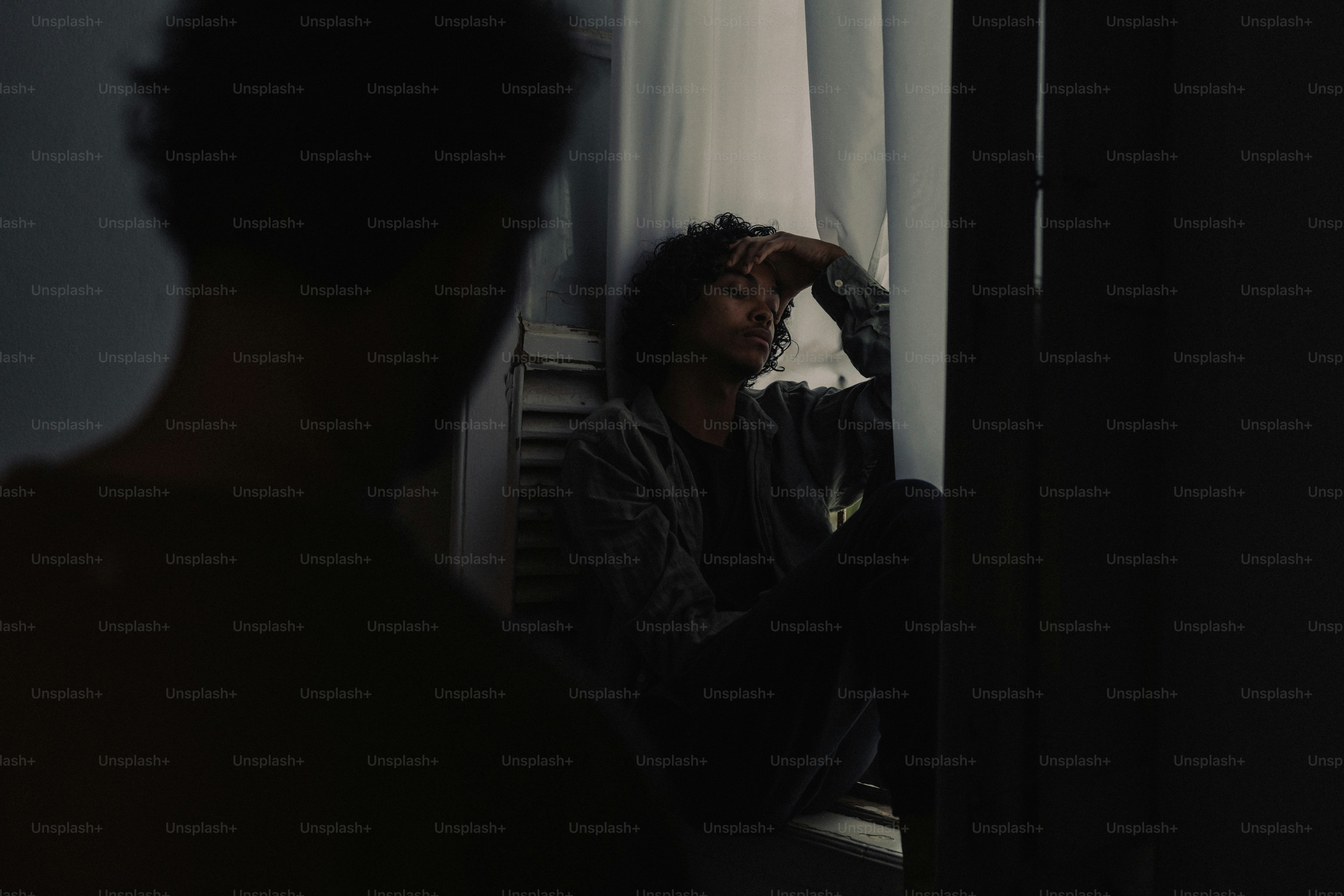 Person sitting by window, another watching in silhouette
