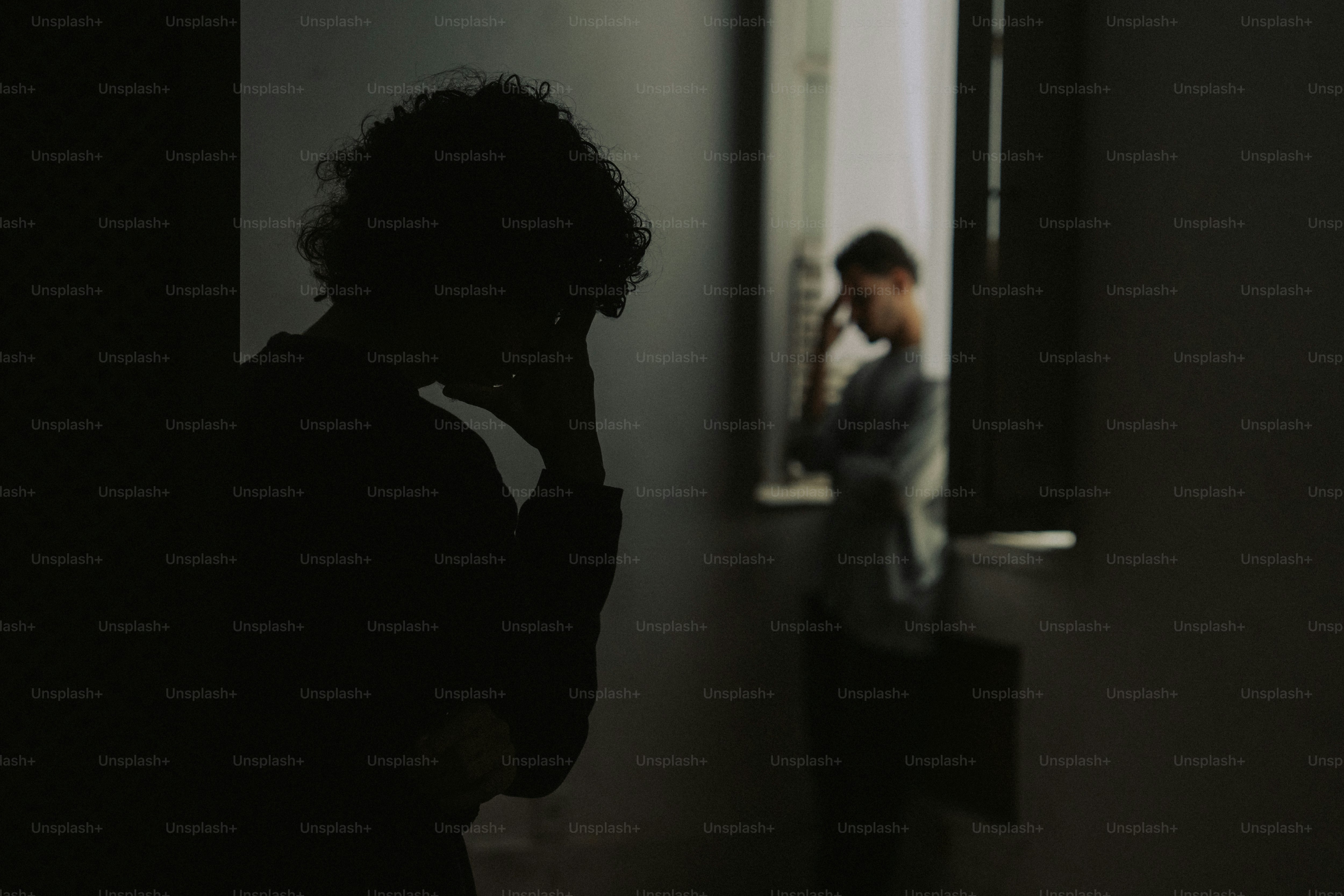 Two people in dark room, one silhouetted, distressed
