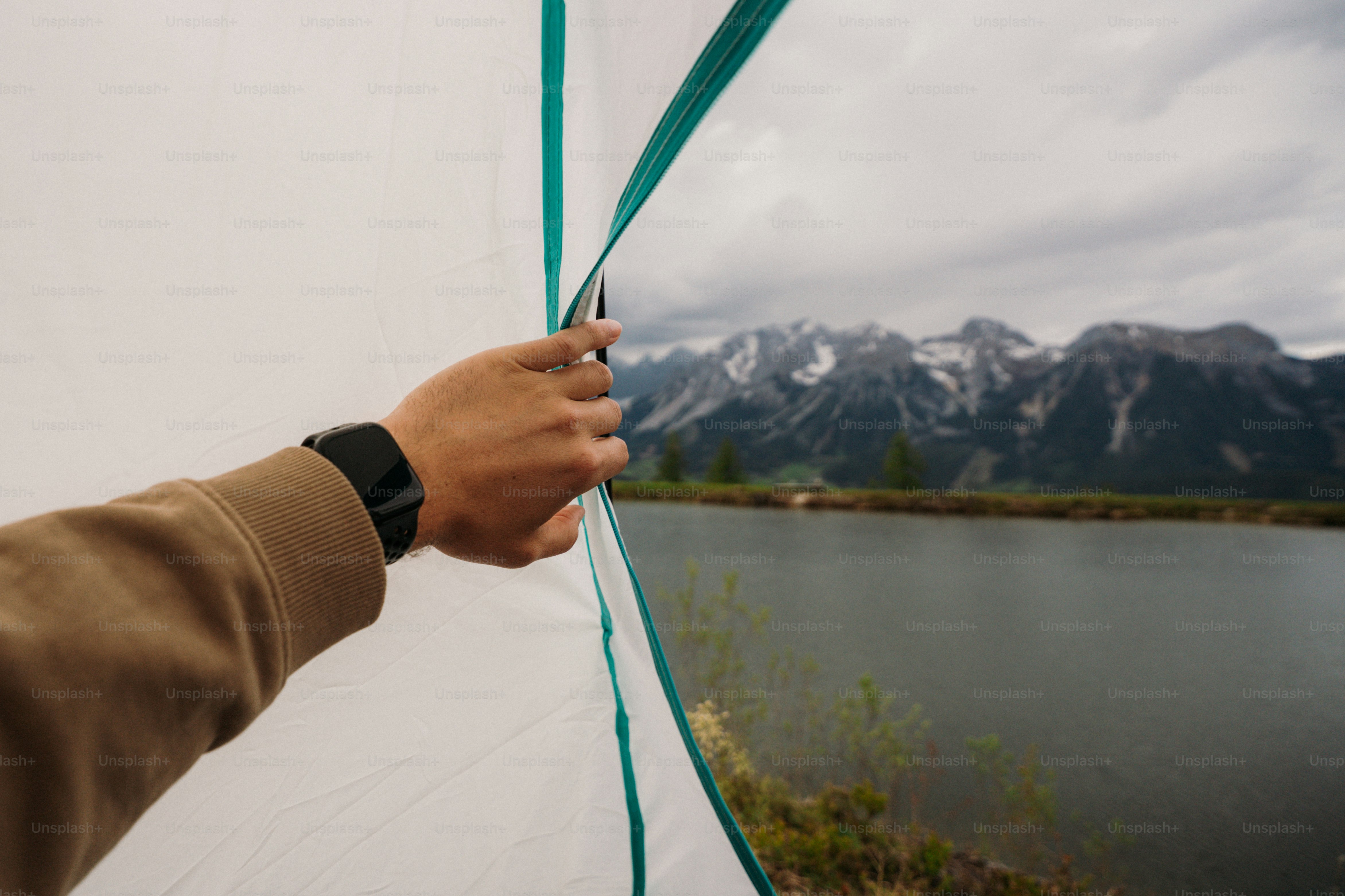 Hand opening tent to lake and cloudy mountains