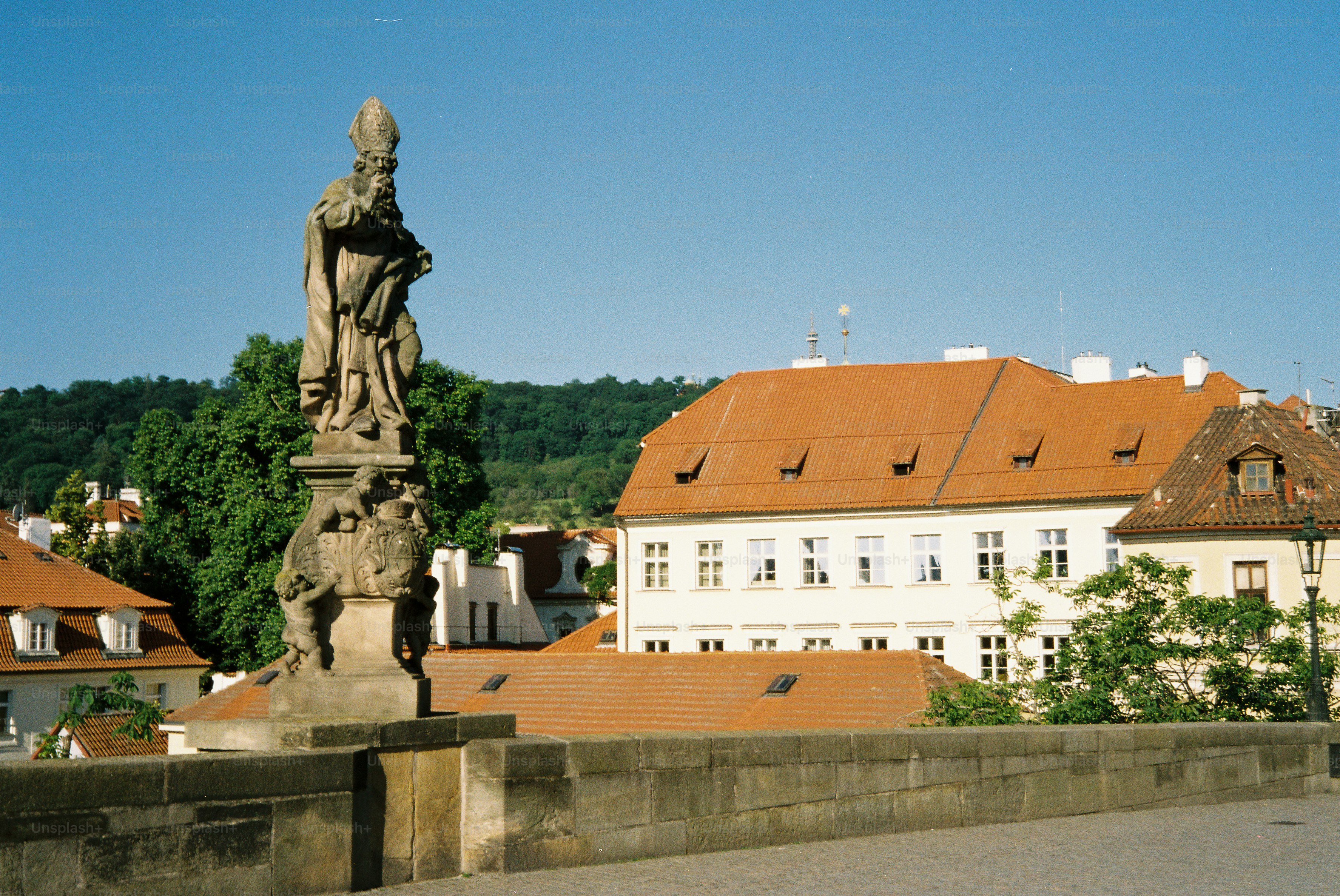 Ornate stone statue on bridge with red-roofed buildings