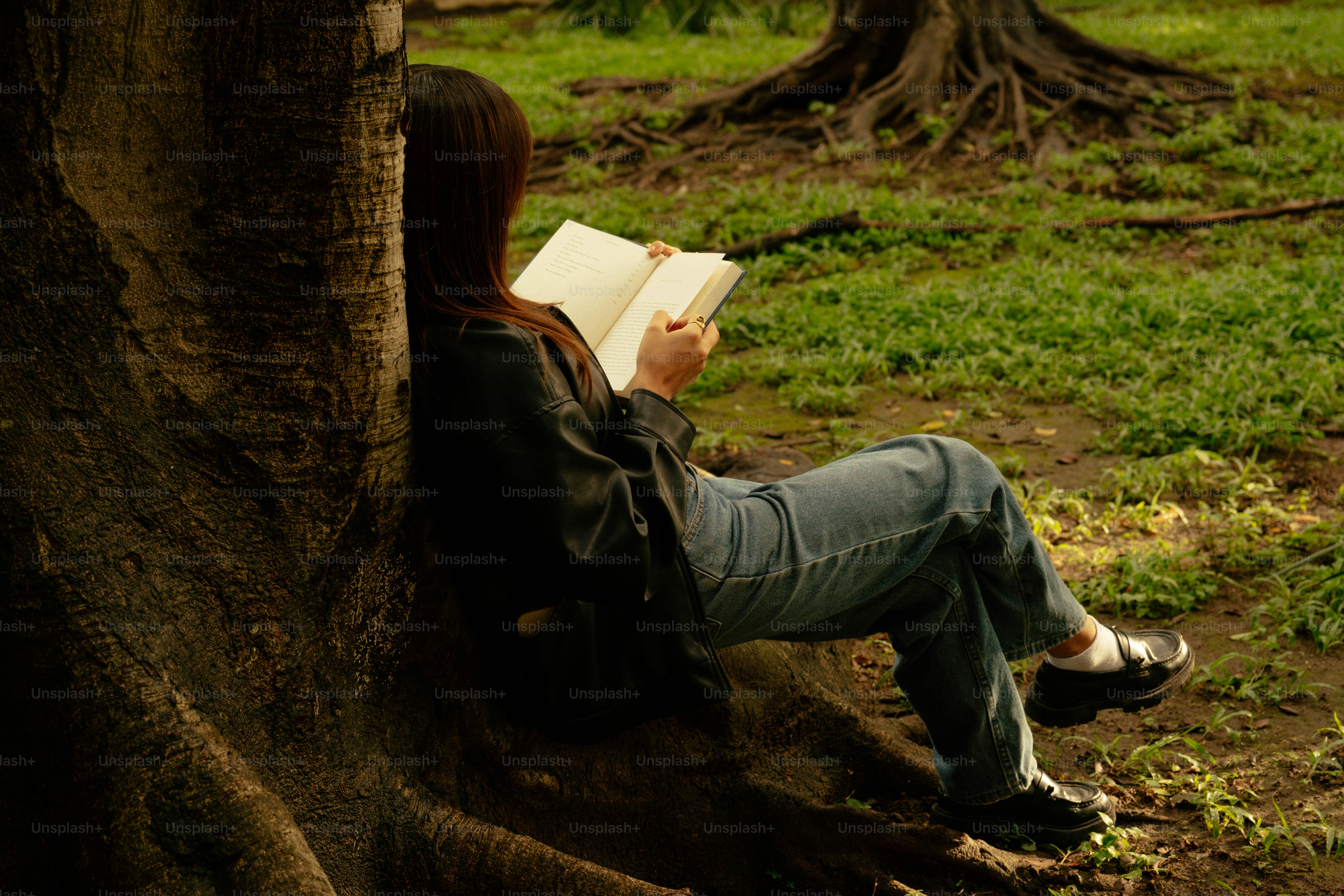 Young woman reading a book against a tree