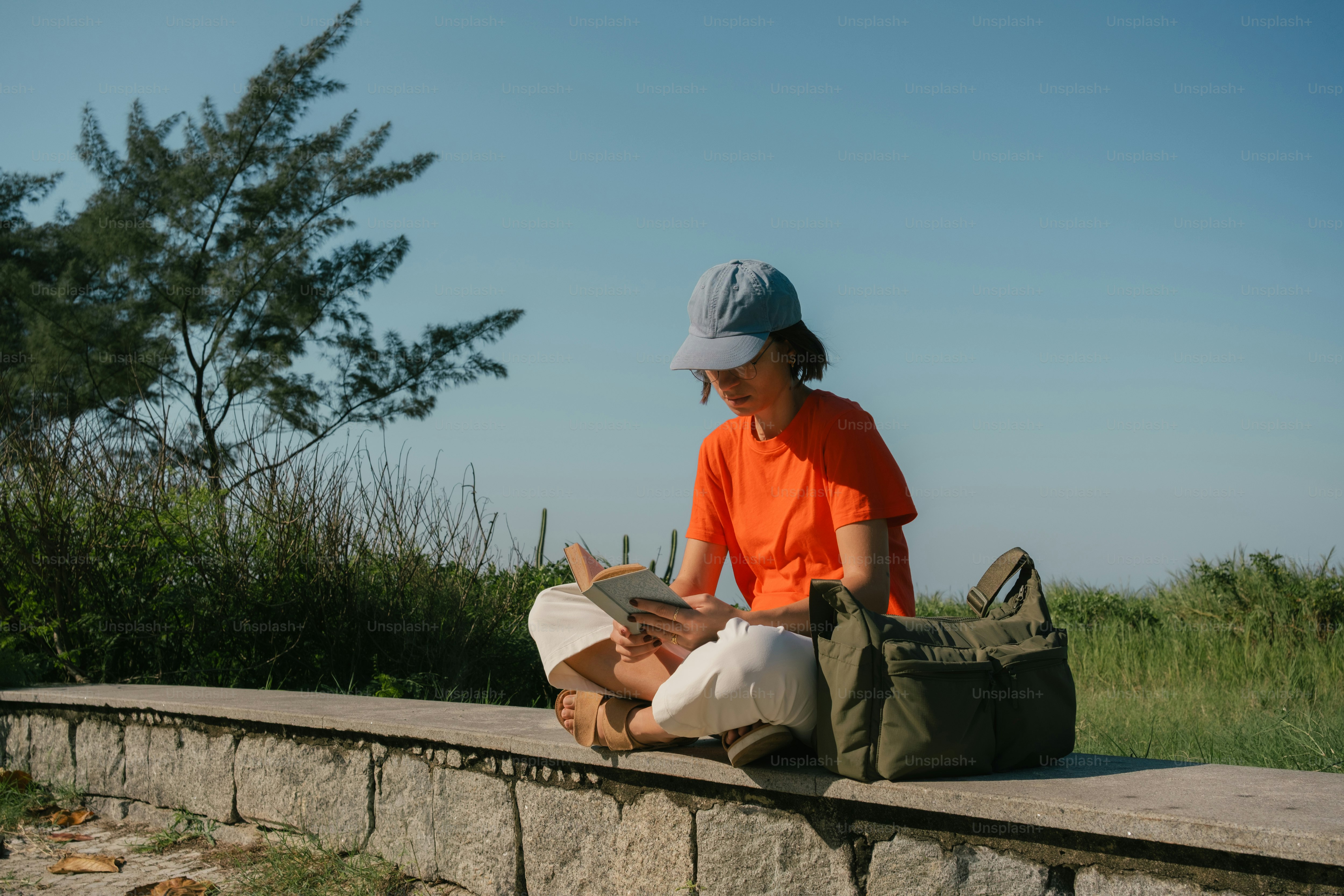 Woman reading book on stone wall outdoors