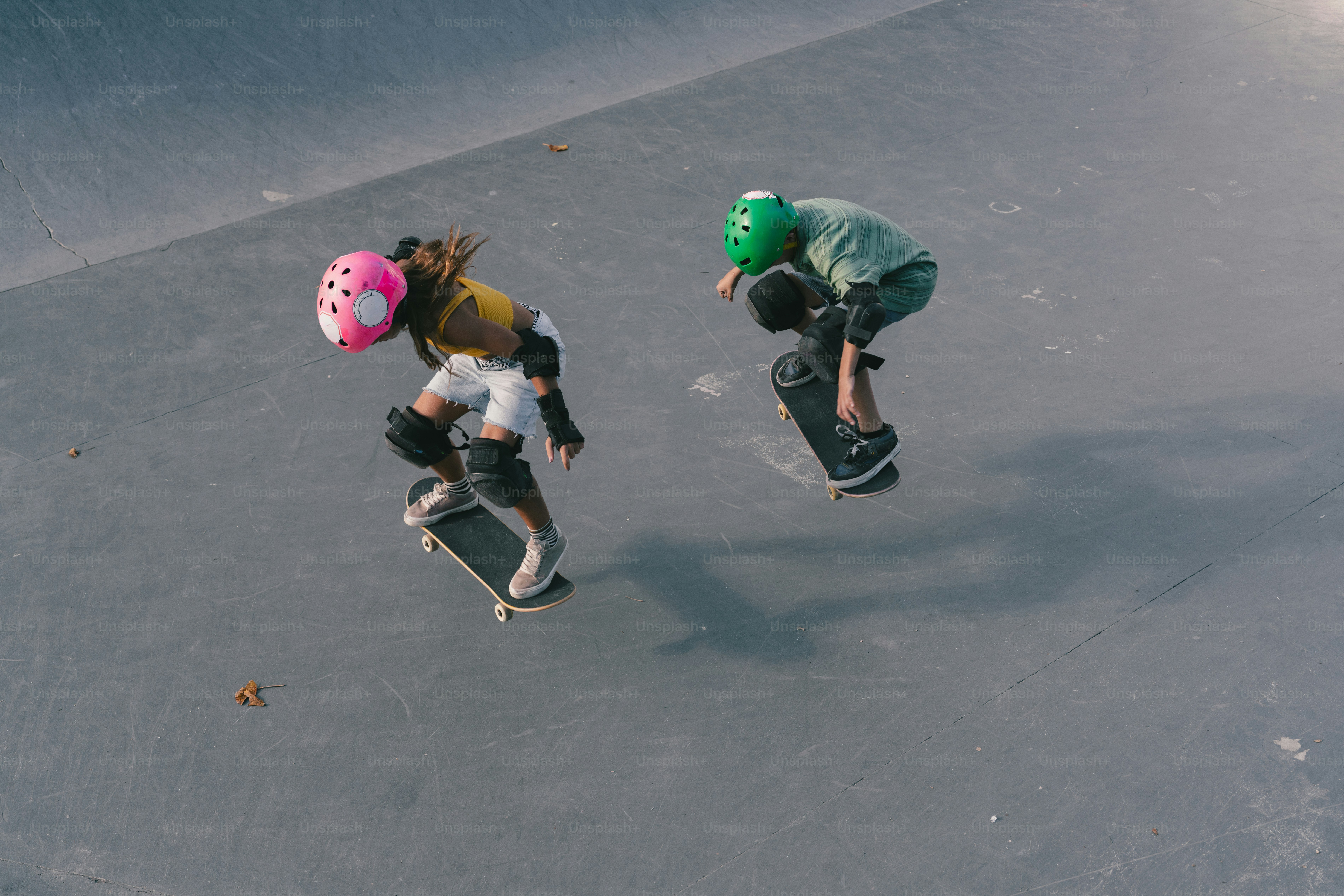 Two skateboarders wearing helmets performing tricks in skatepark