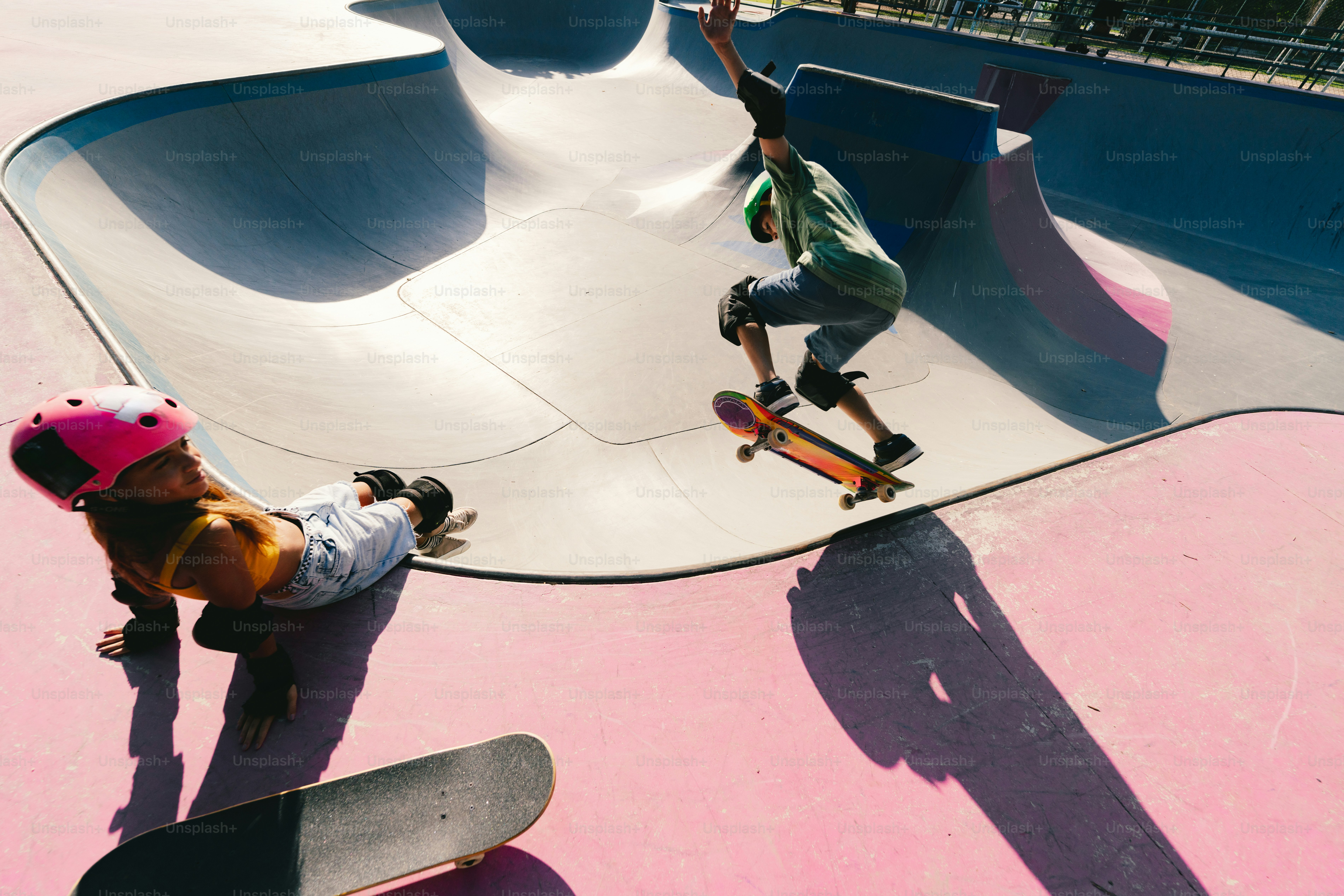 Skateboarder jumps while another rests in pink skatepark