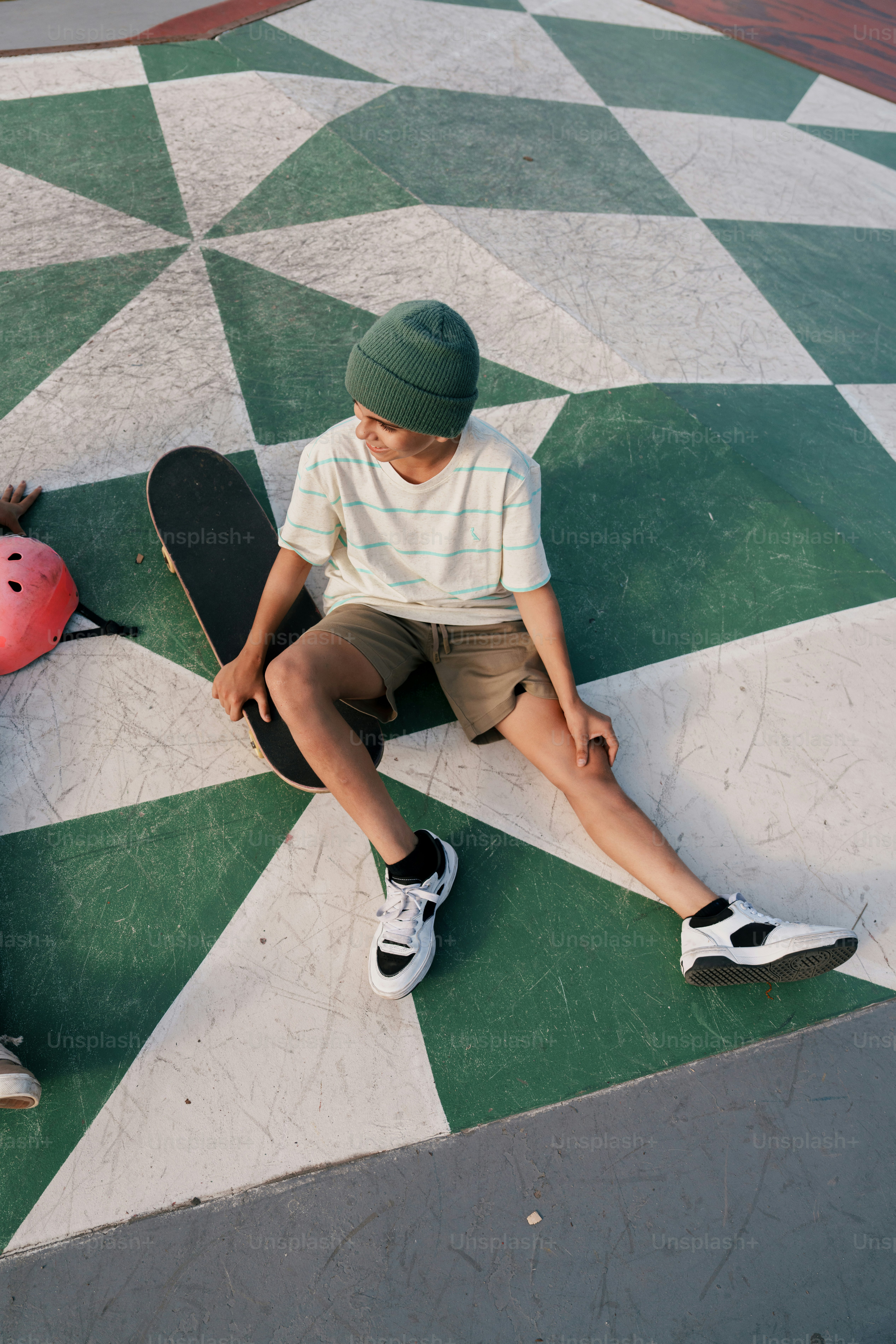 Boy sitting on skateboard in checkered skatepark