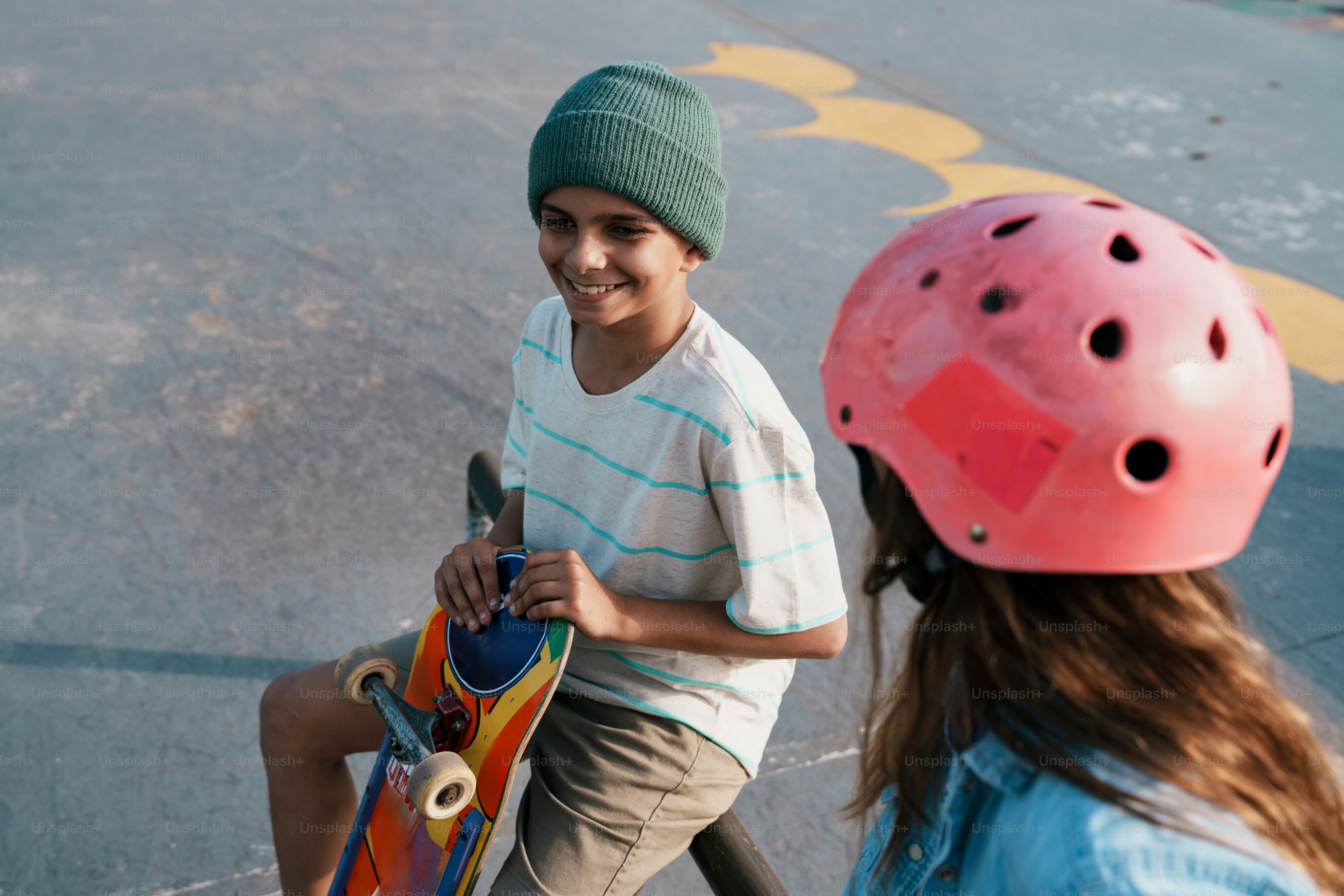 Boy with skateboard smiling at person in pink helmet