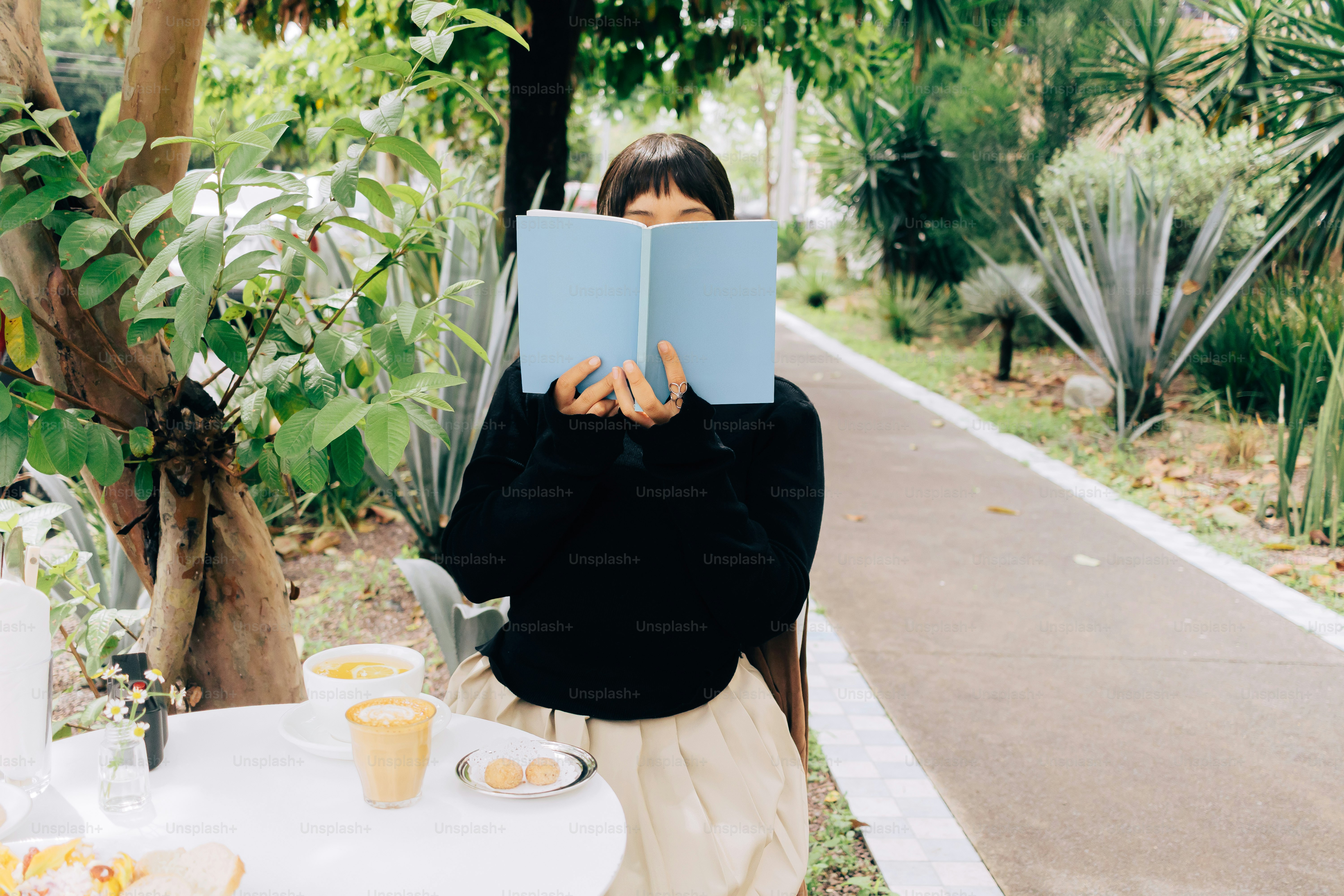 Frau hält blaues Buch und bedeckt Gesicht im Garten