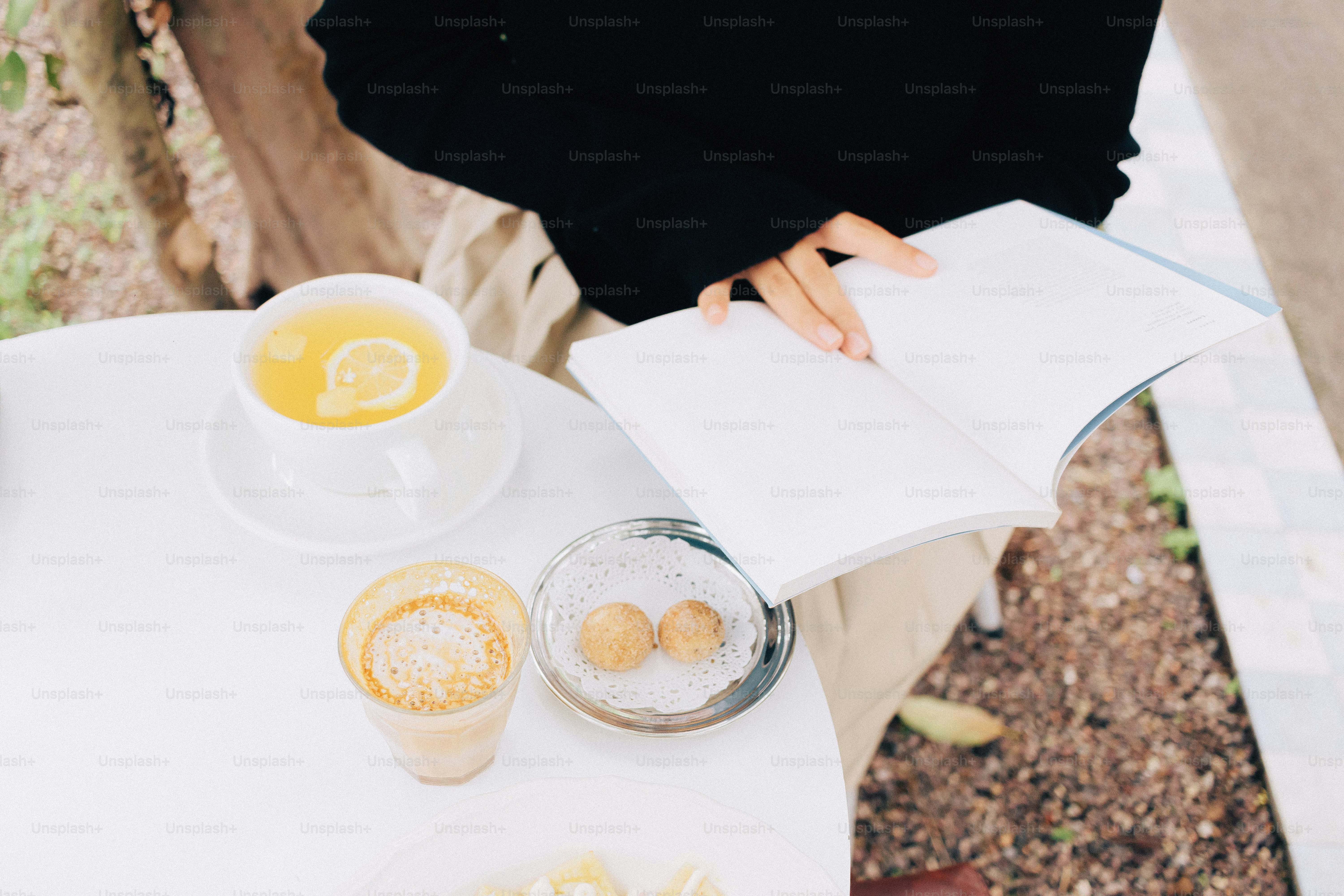 Person liest draußen ein Buch mit Tee und Snacks