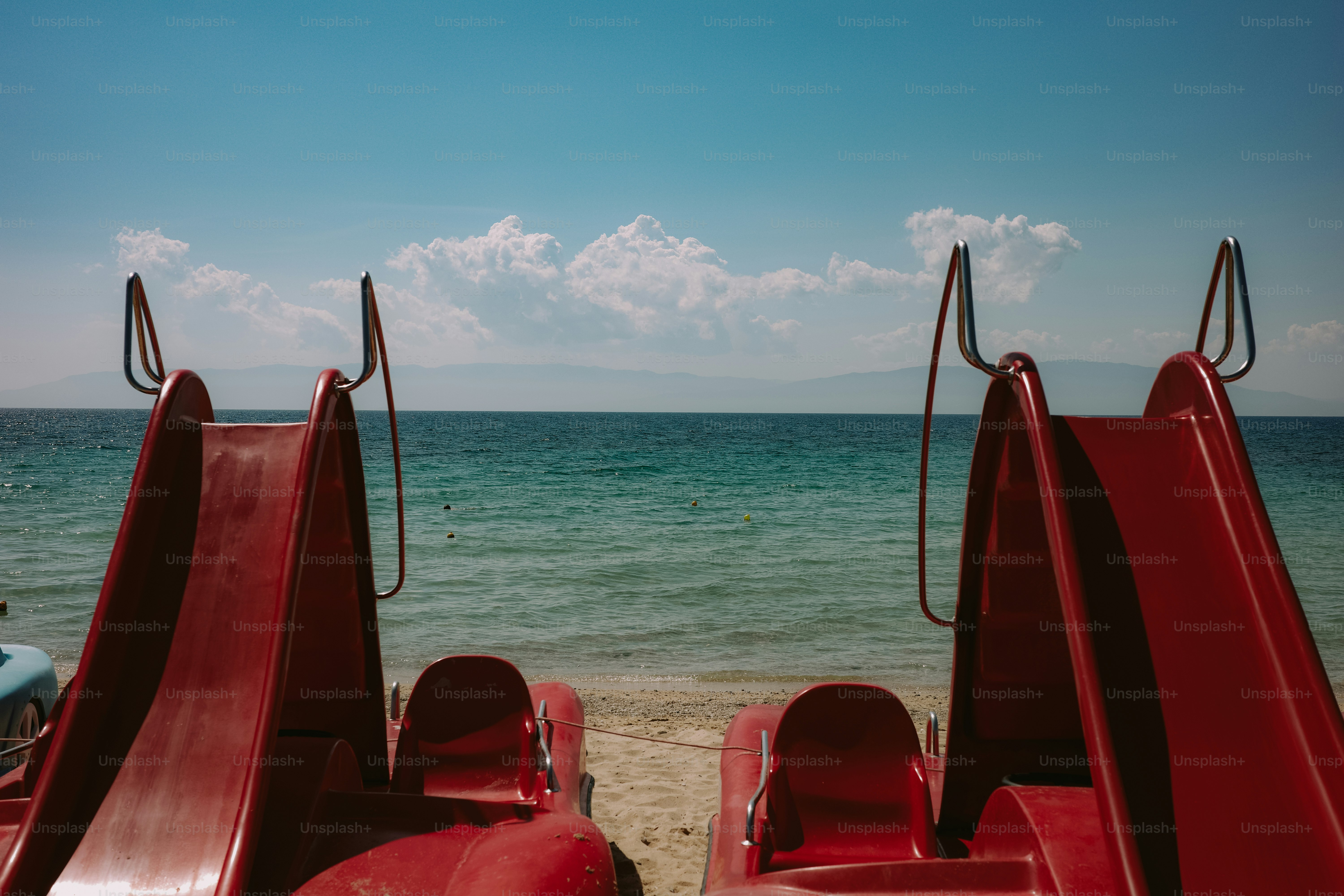 Red pedal boats on sandy beach, calm blue sea