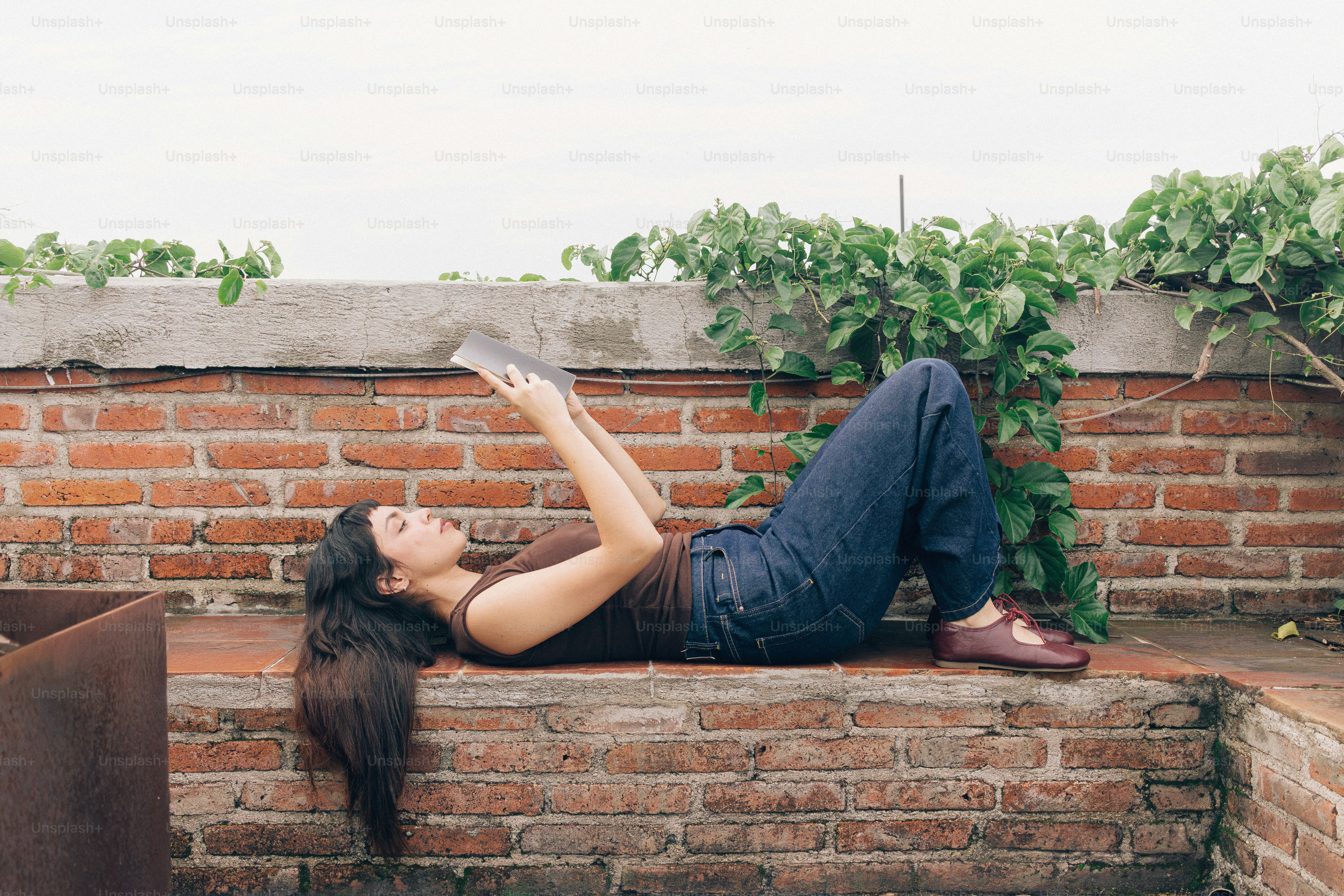 Young woman lying on brick wall reading book