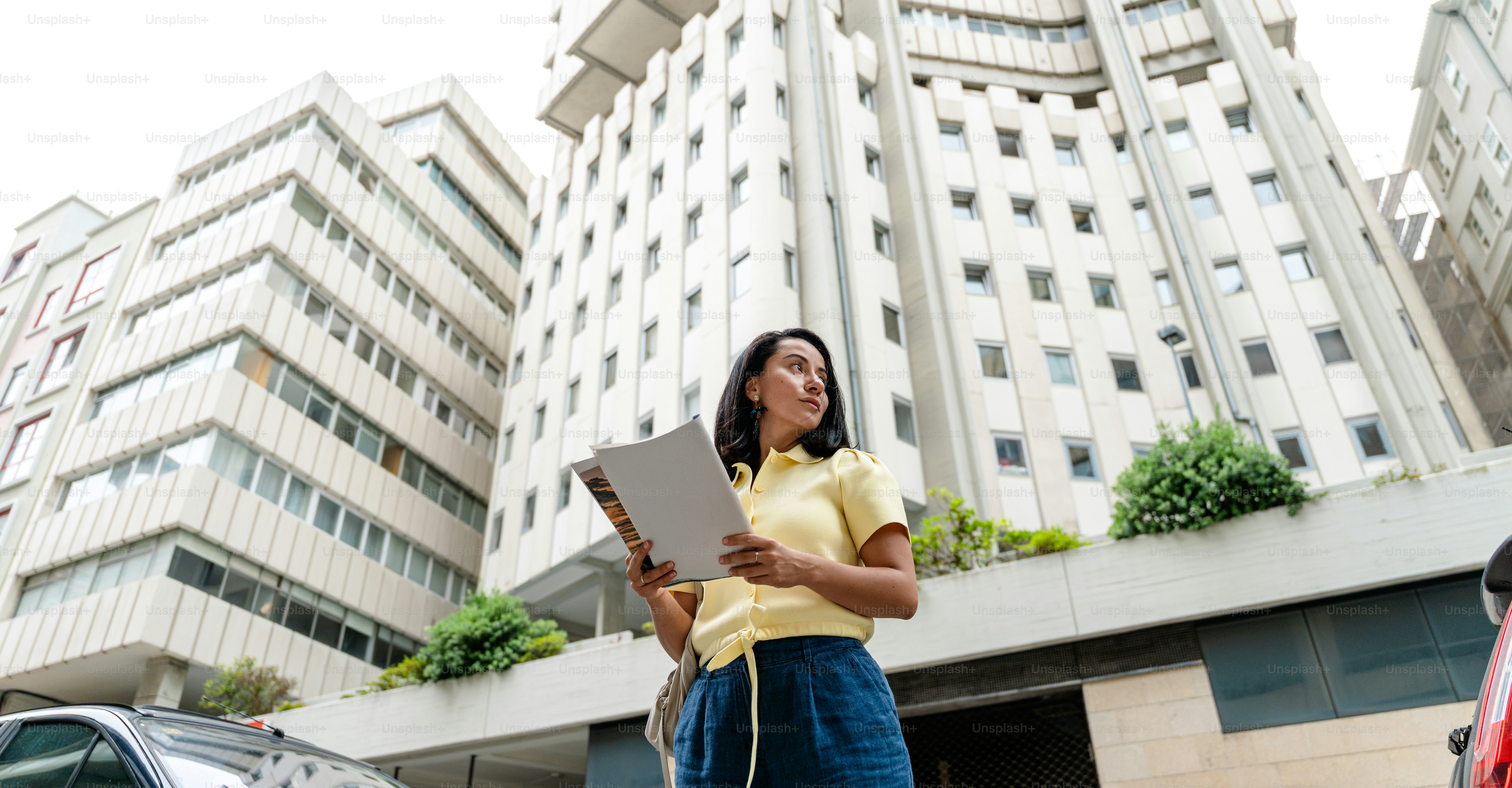Woman with papers looking up at modern buildings