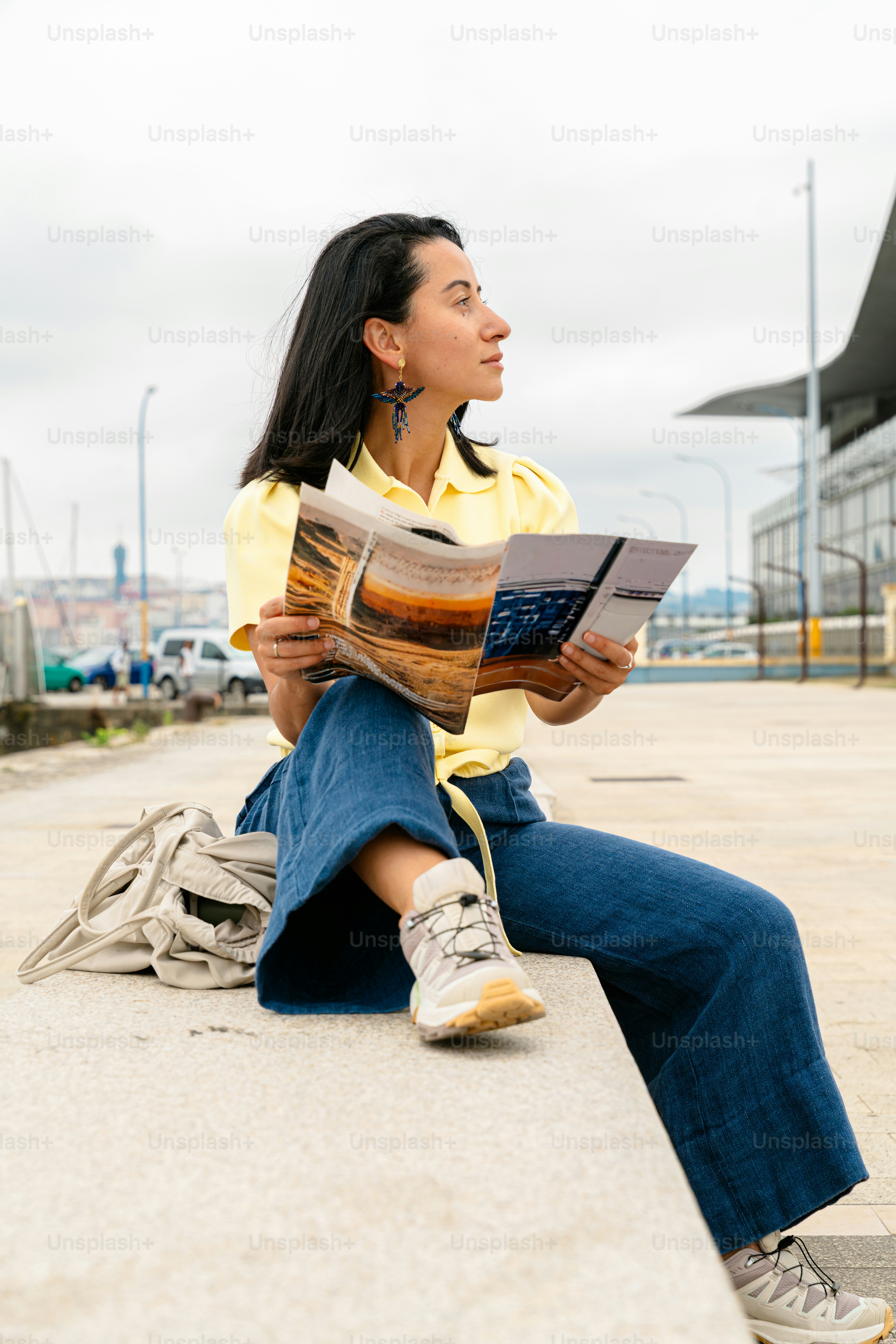 Woman sitting outdoors holding brochure, looking aside