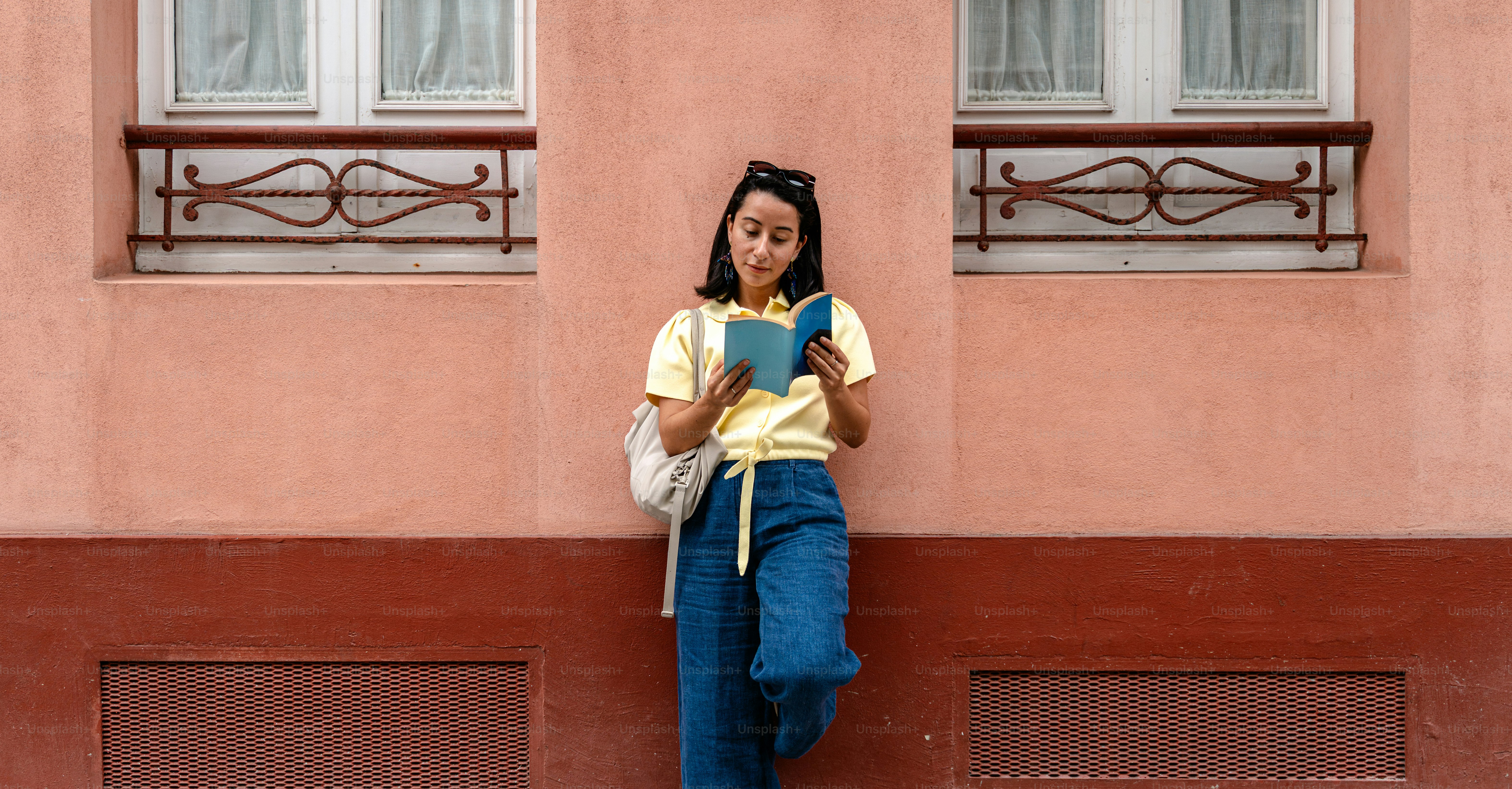 Young woman reading a book against a pink wall