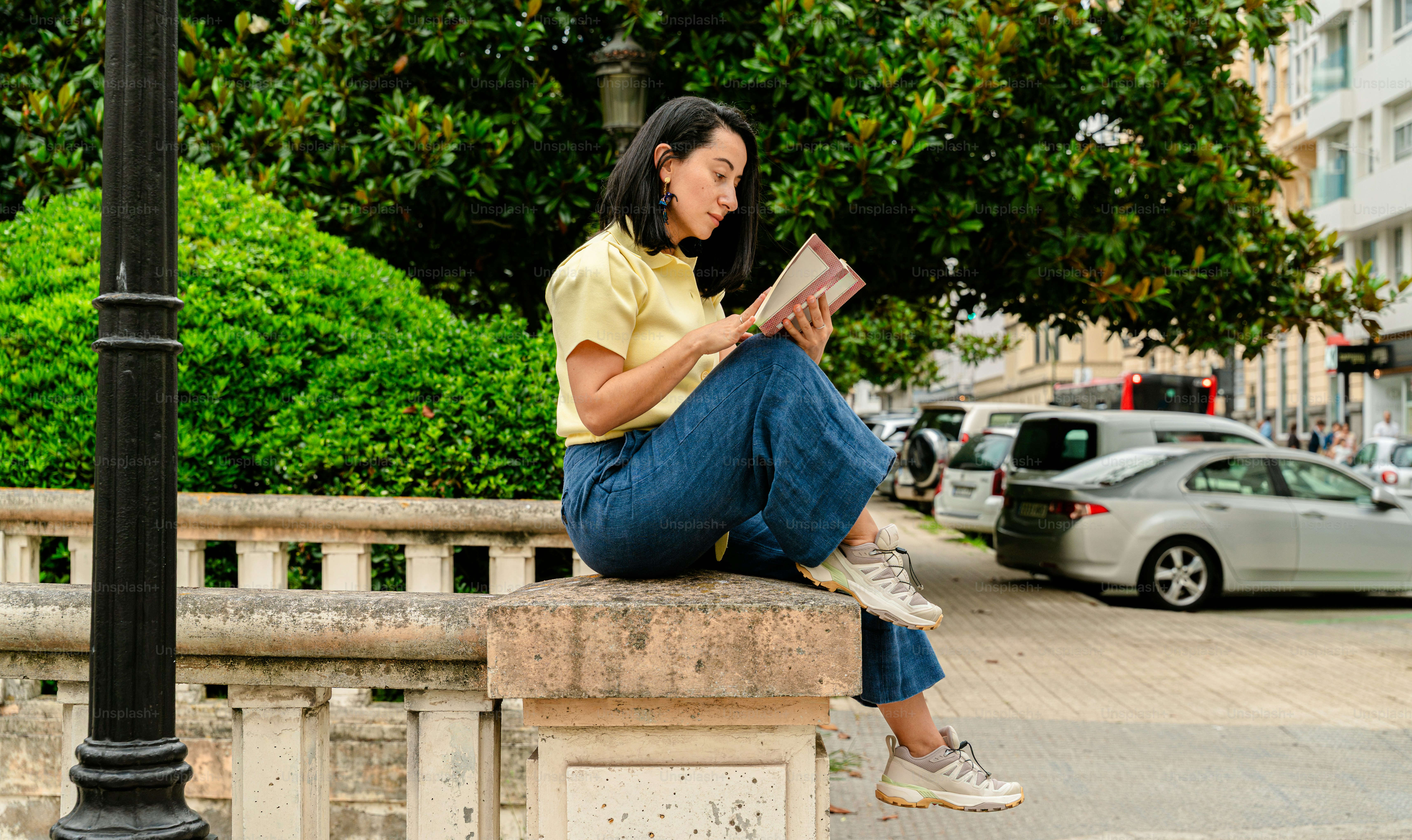 Woman reading newspaper sitting on stone pillar