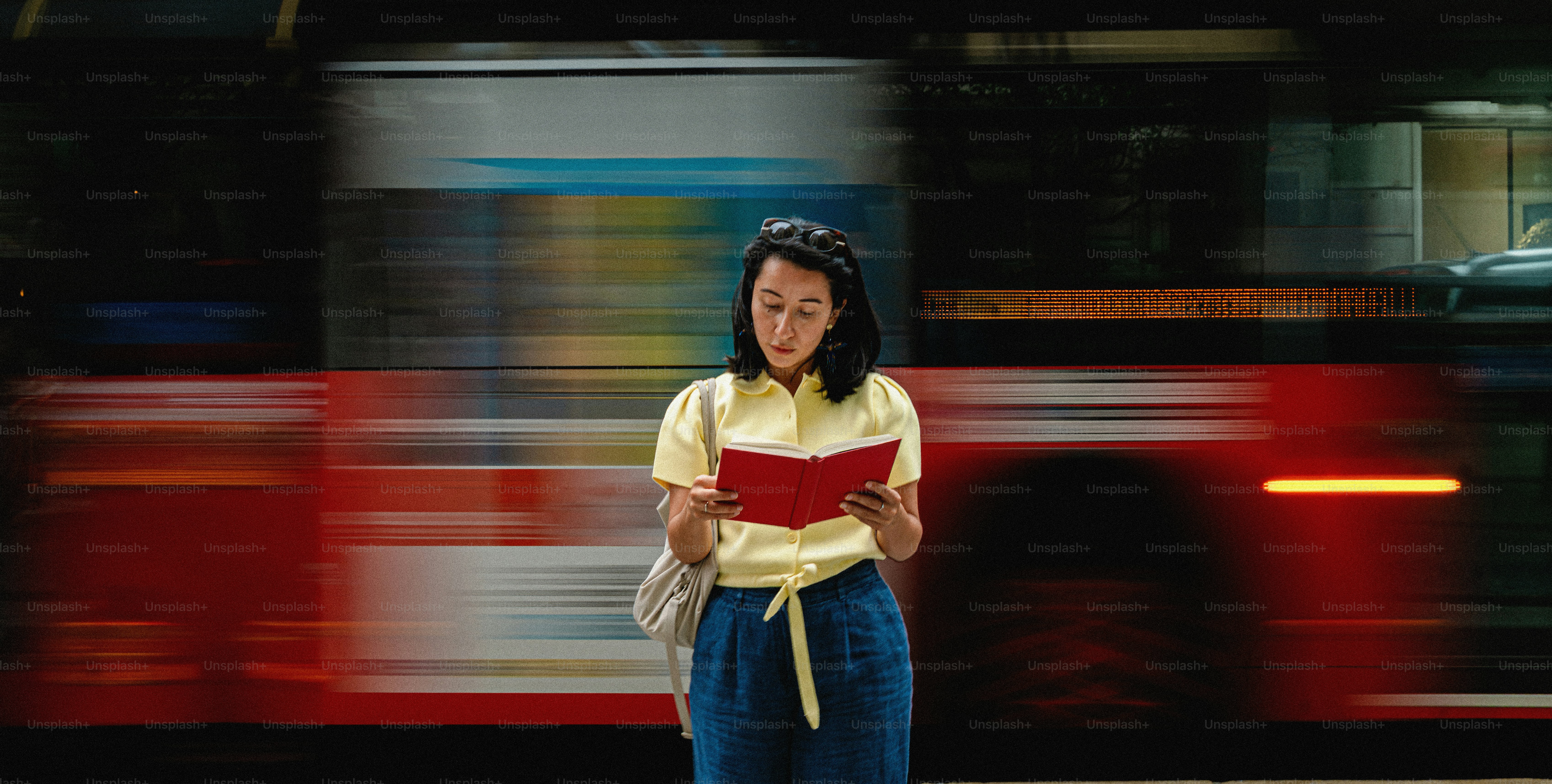 Woman reading book as blurred red bus passes