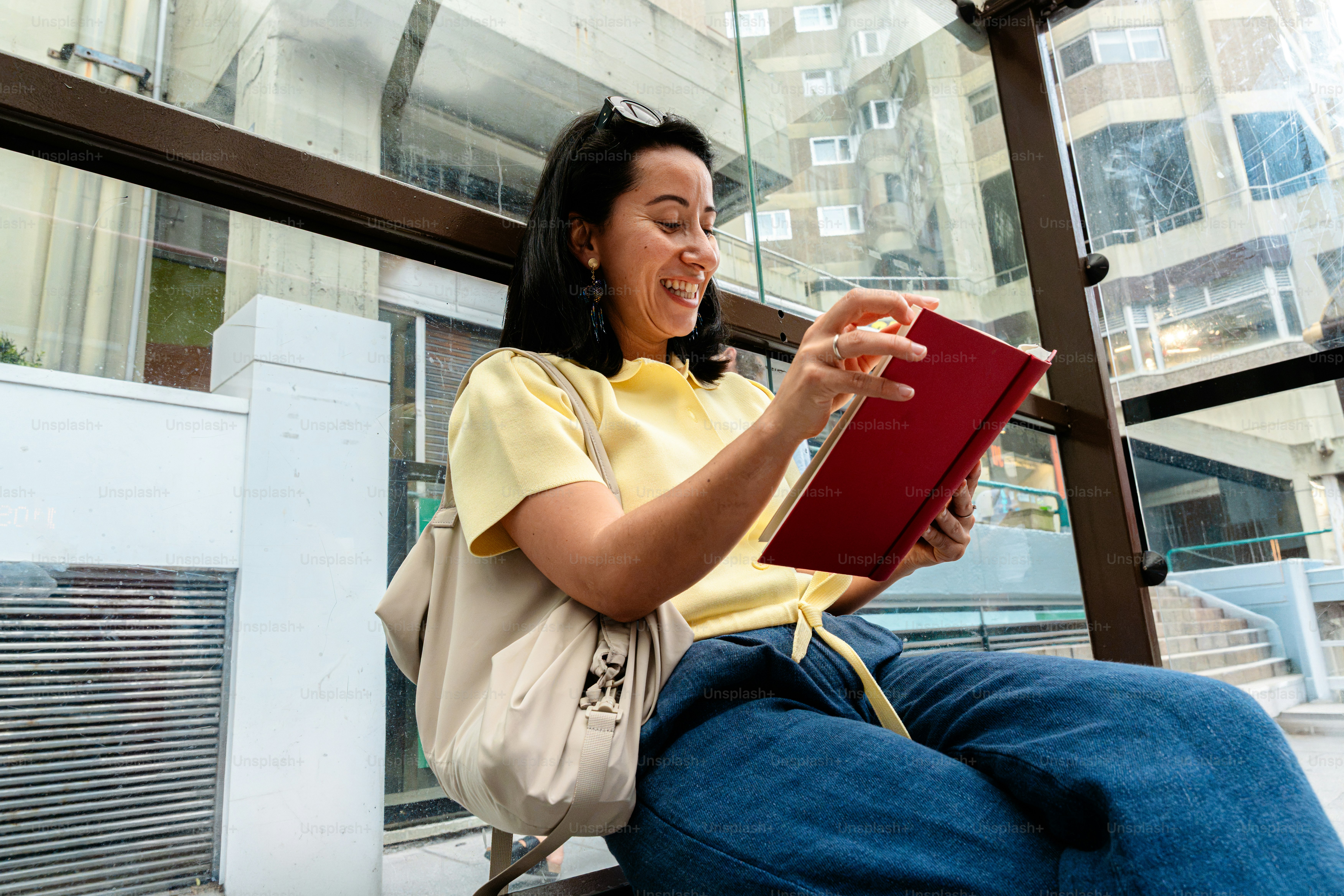 Smiling woman reading red book at bus stop
