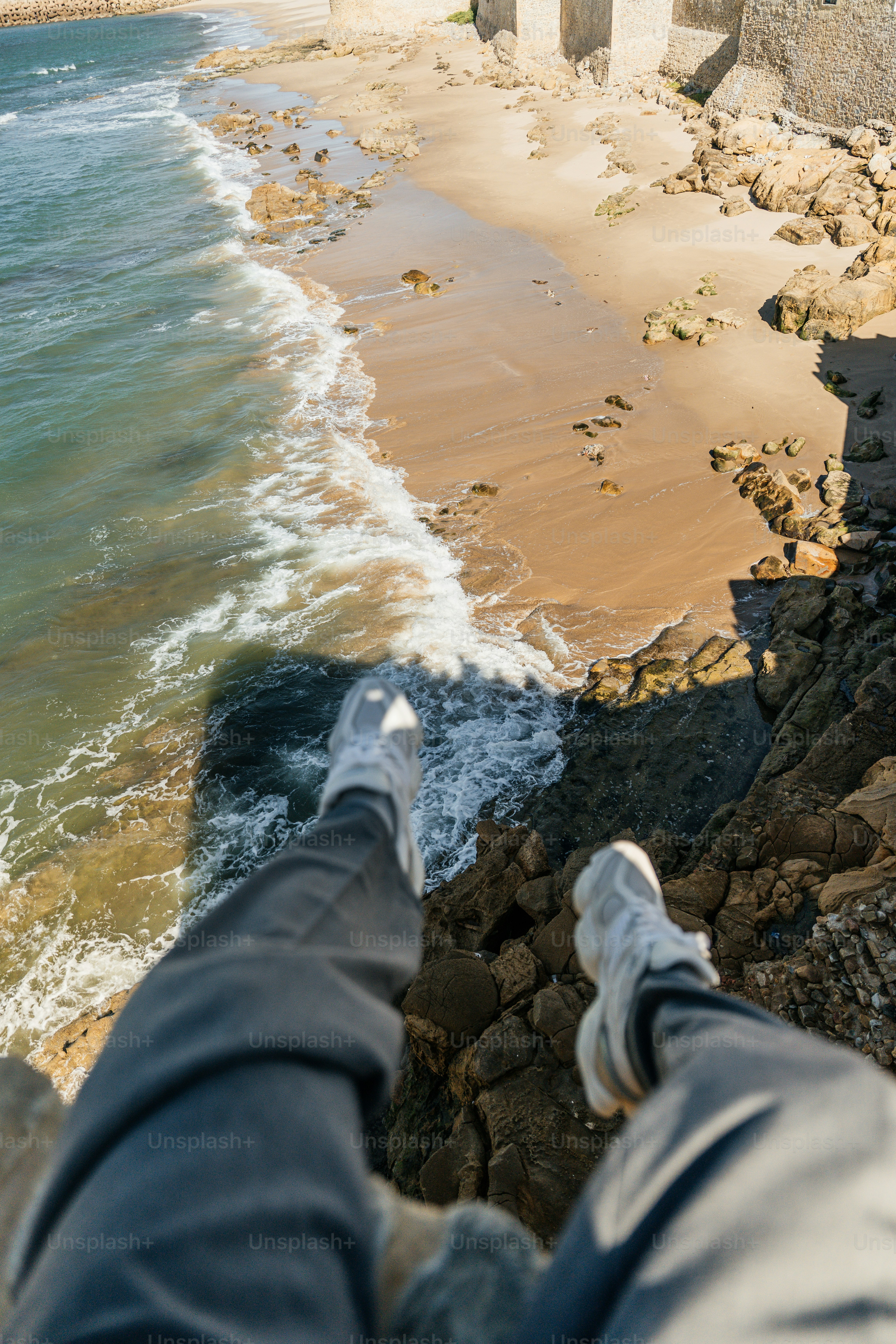 Legs dangling over cliff edge above sandy beach