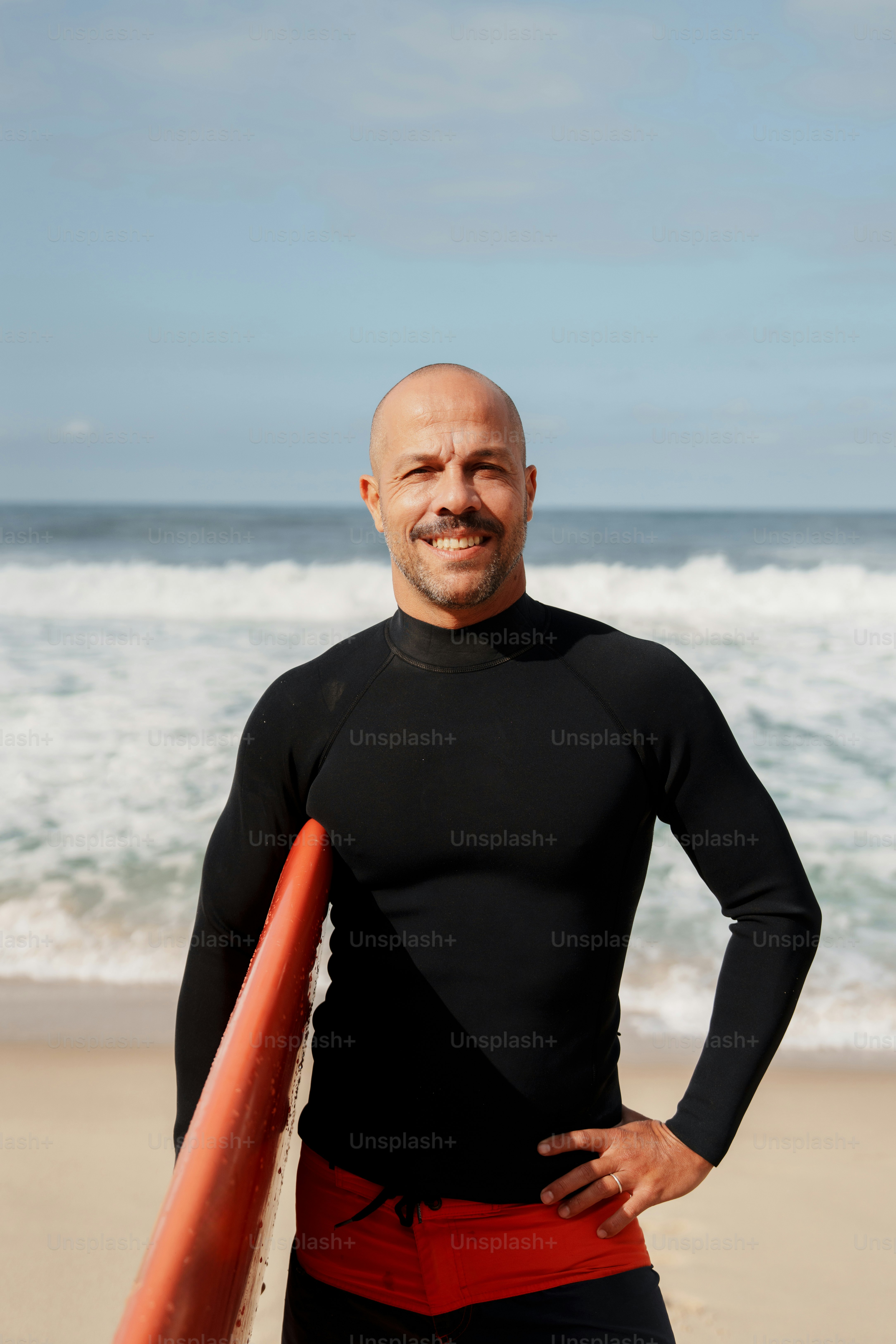 Smiling surfer holding orange board on sunny beach