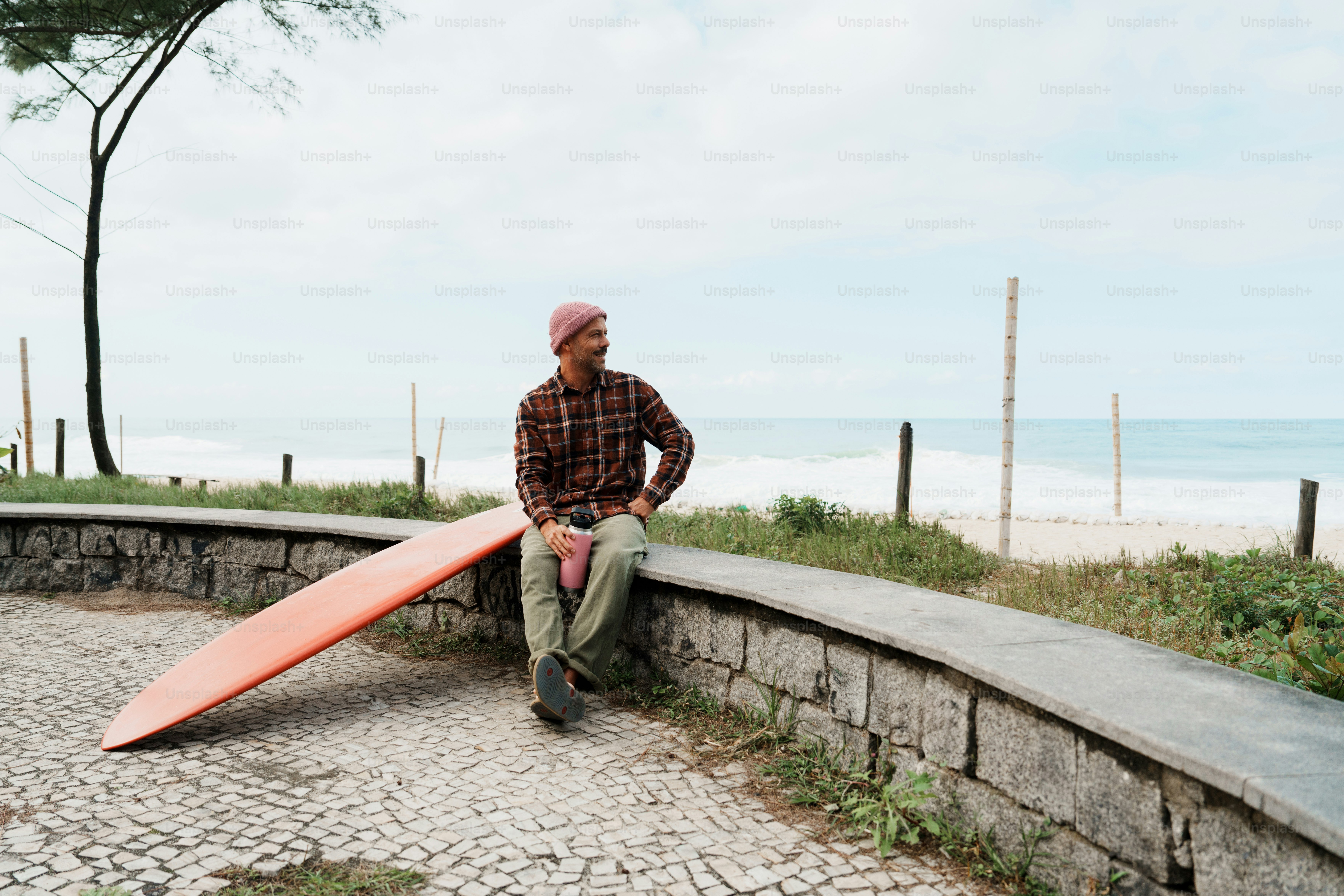 Man with surfboard sitting on wall by beach