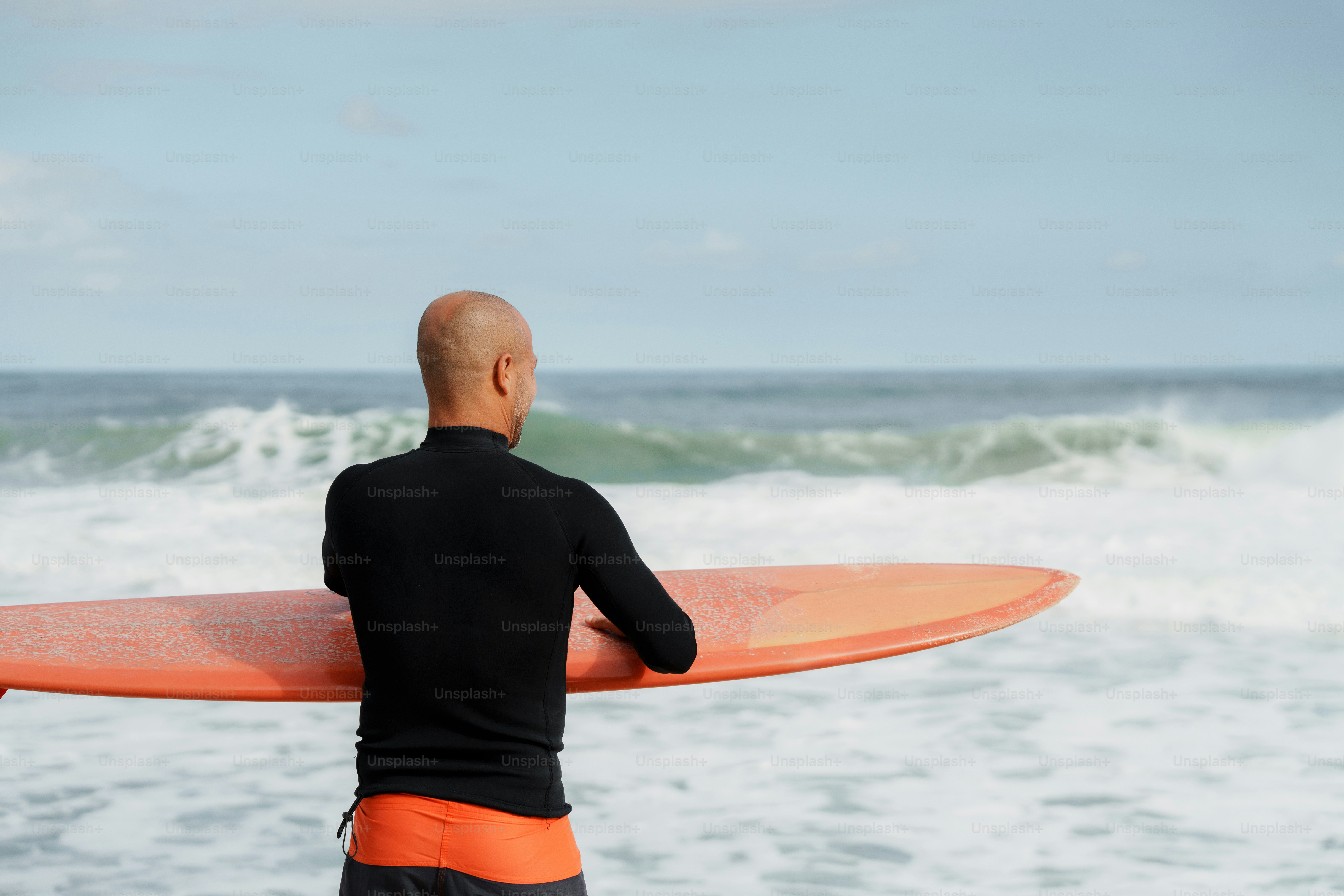 Surfer with orange board watching ocean waves