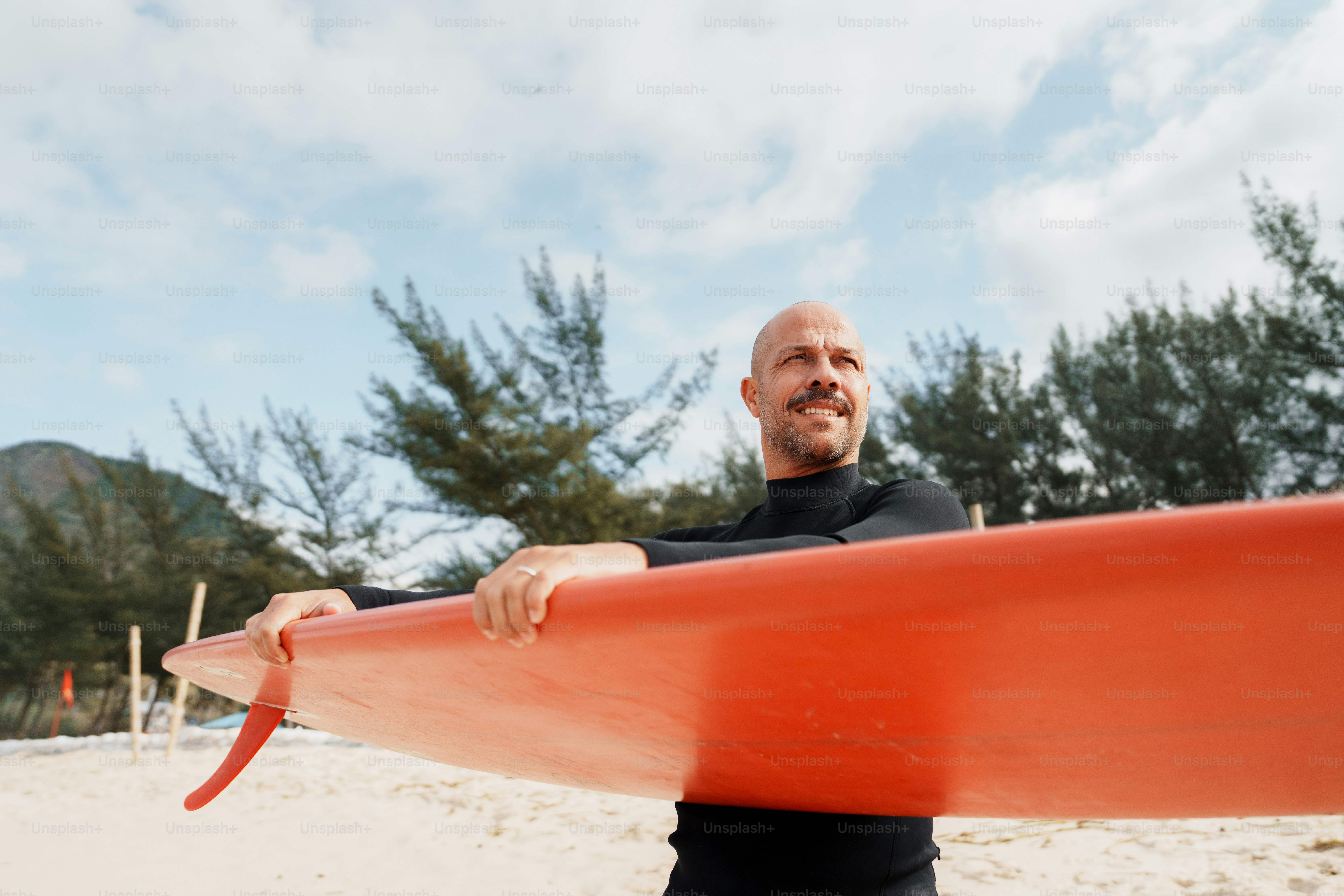Surfer in wetsuit holding red surfboard on beach