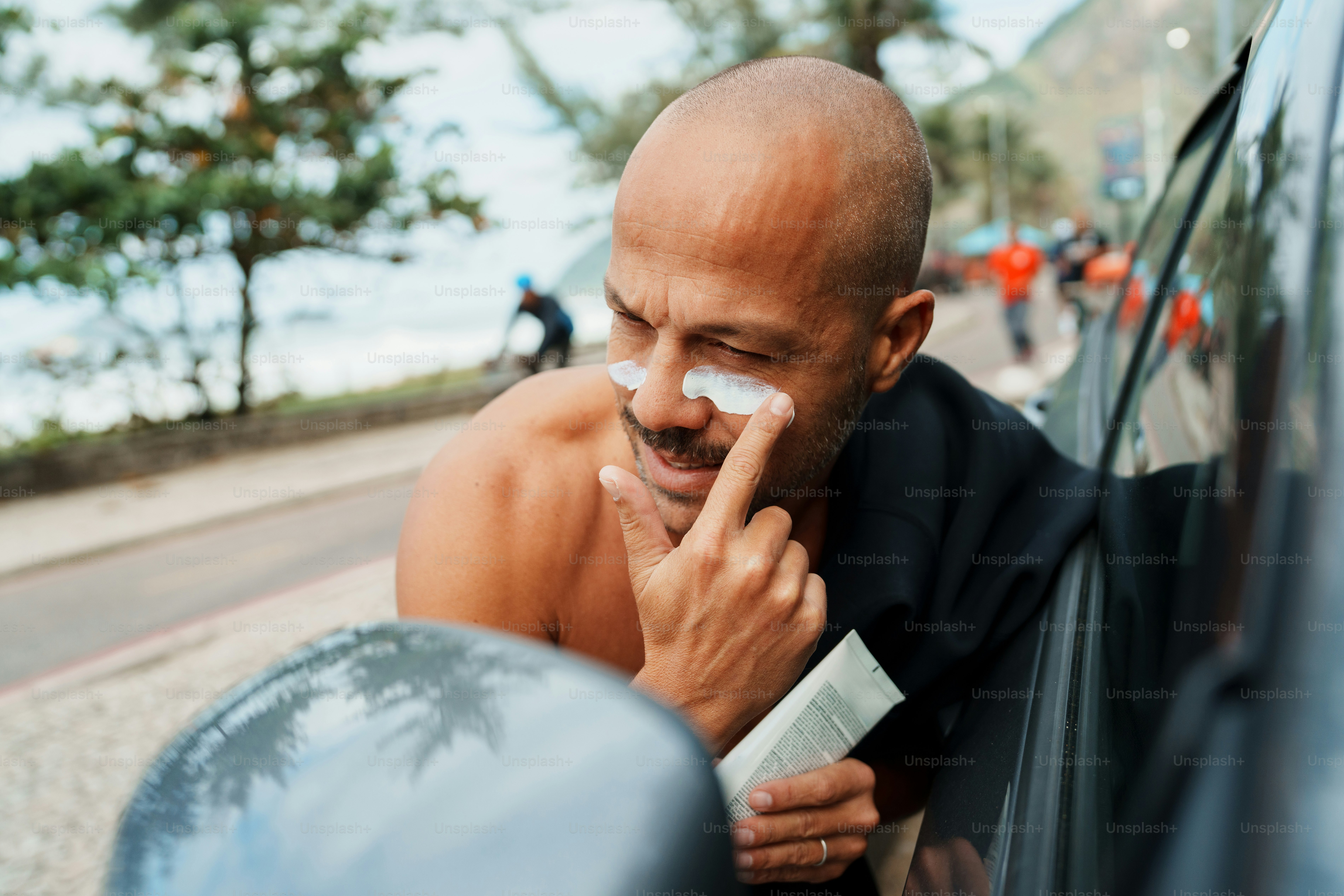 Bald man applying sunscreen to his face outdoors