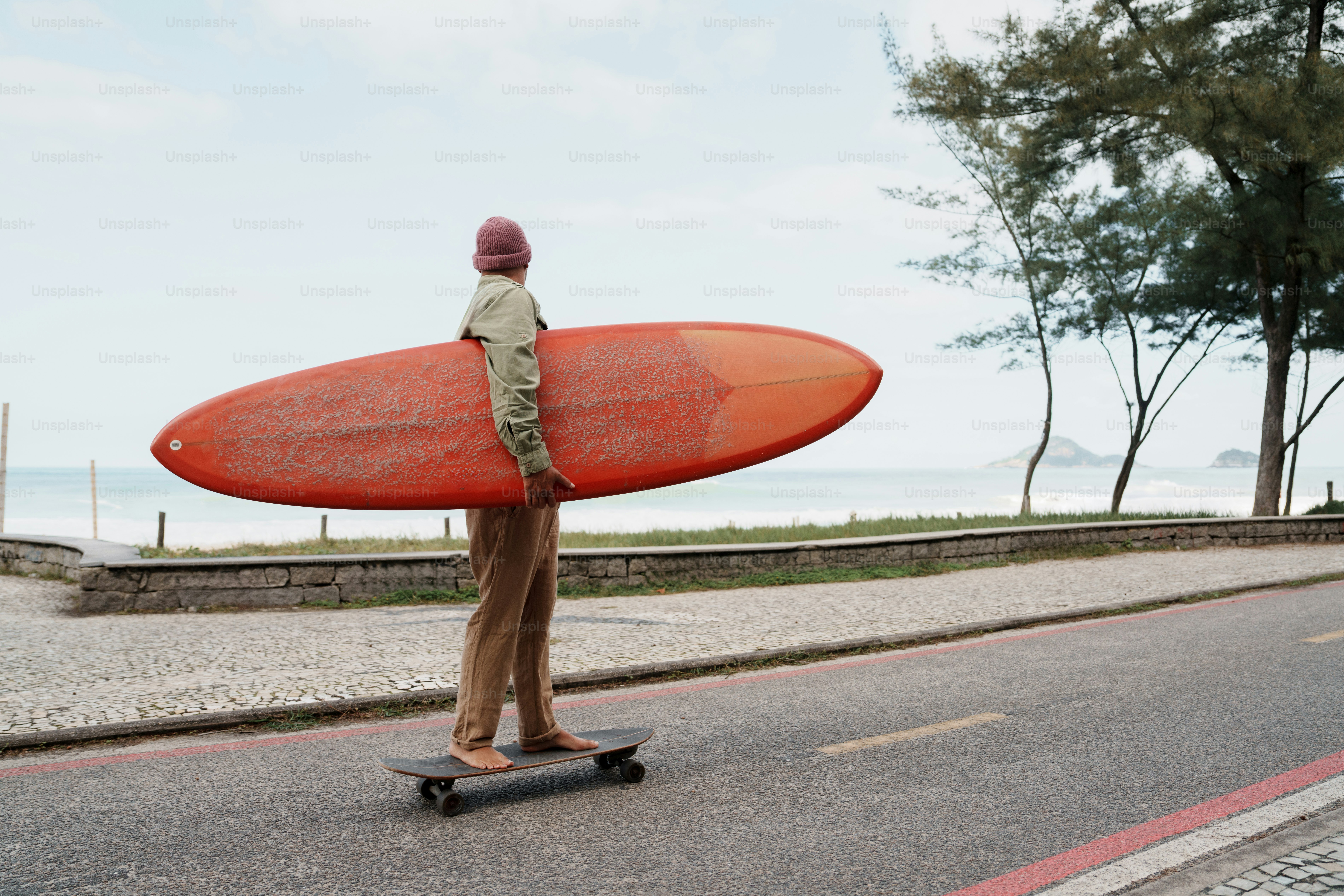 Surfer carrying orange surfboard on skateboard by ocean