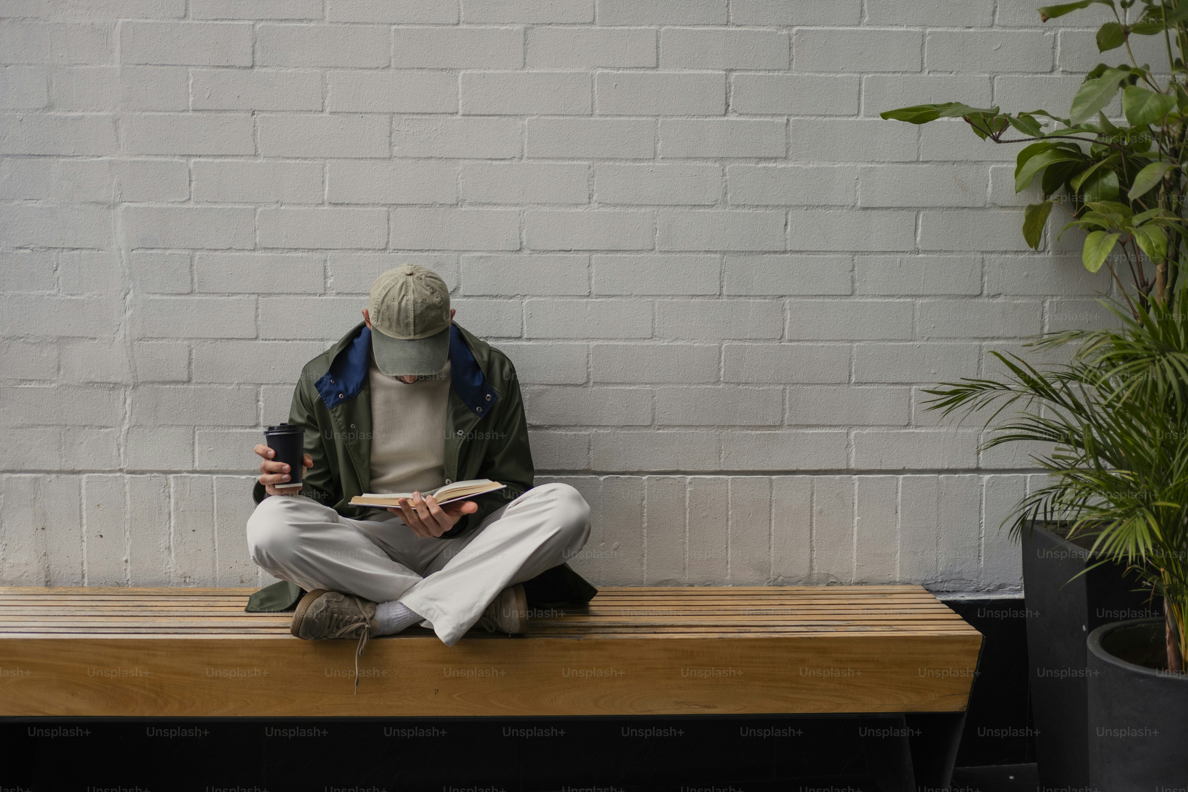 Person in cap reading book on a wooden bench