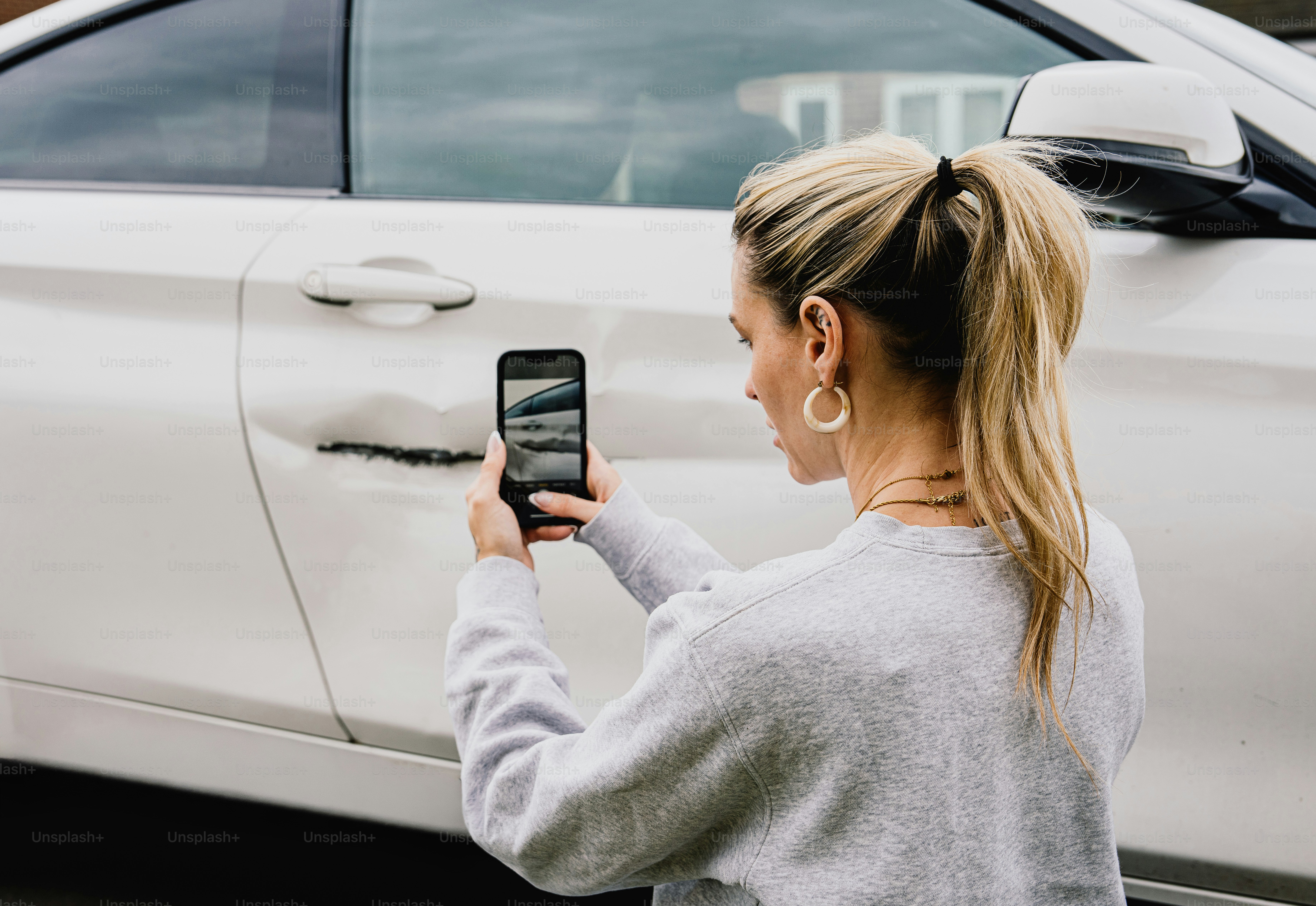 Woman photographing dent and scratch on white car