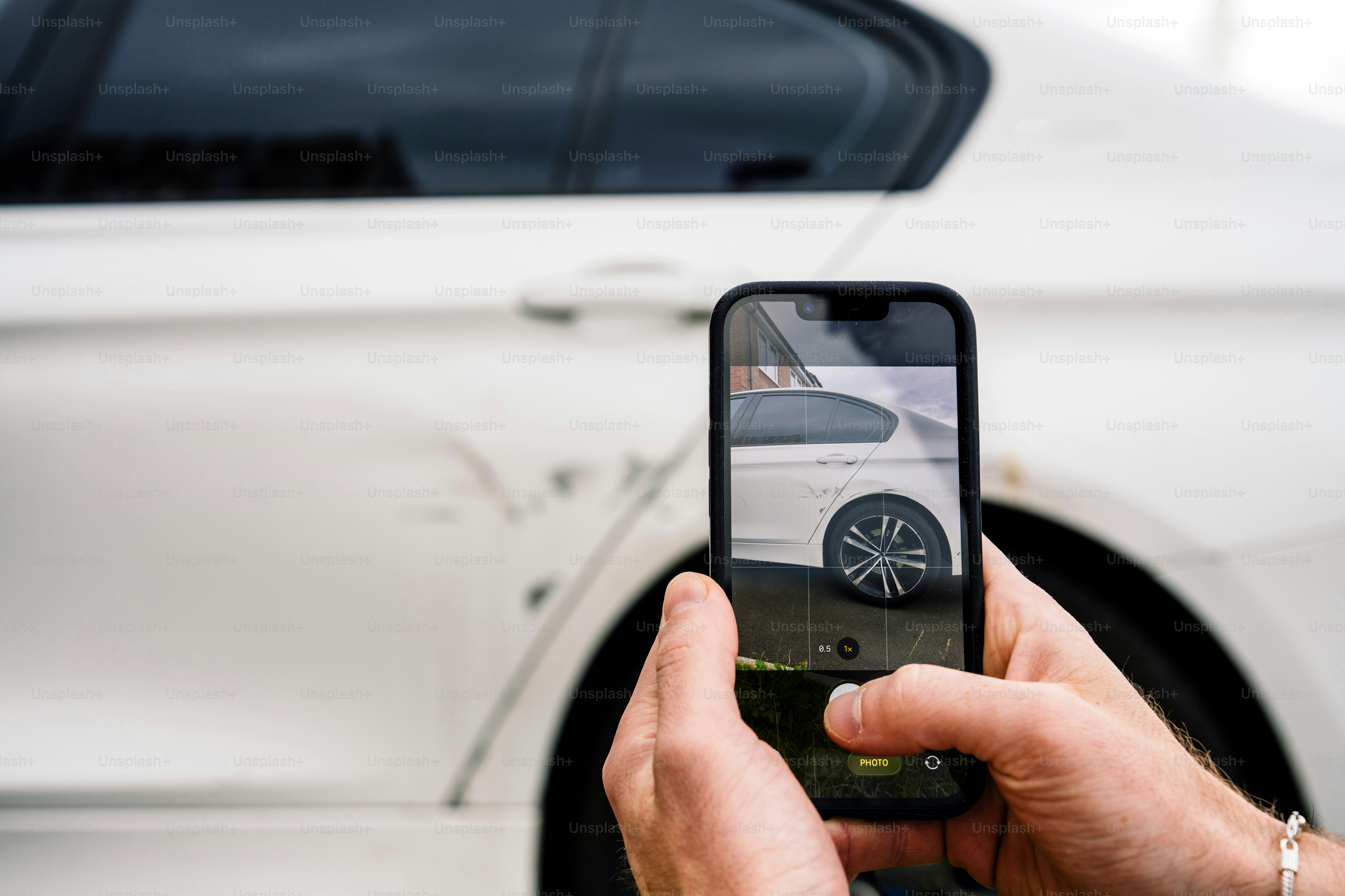 Hands taking smartphone picture of damaged white car