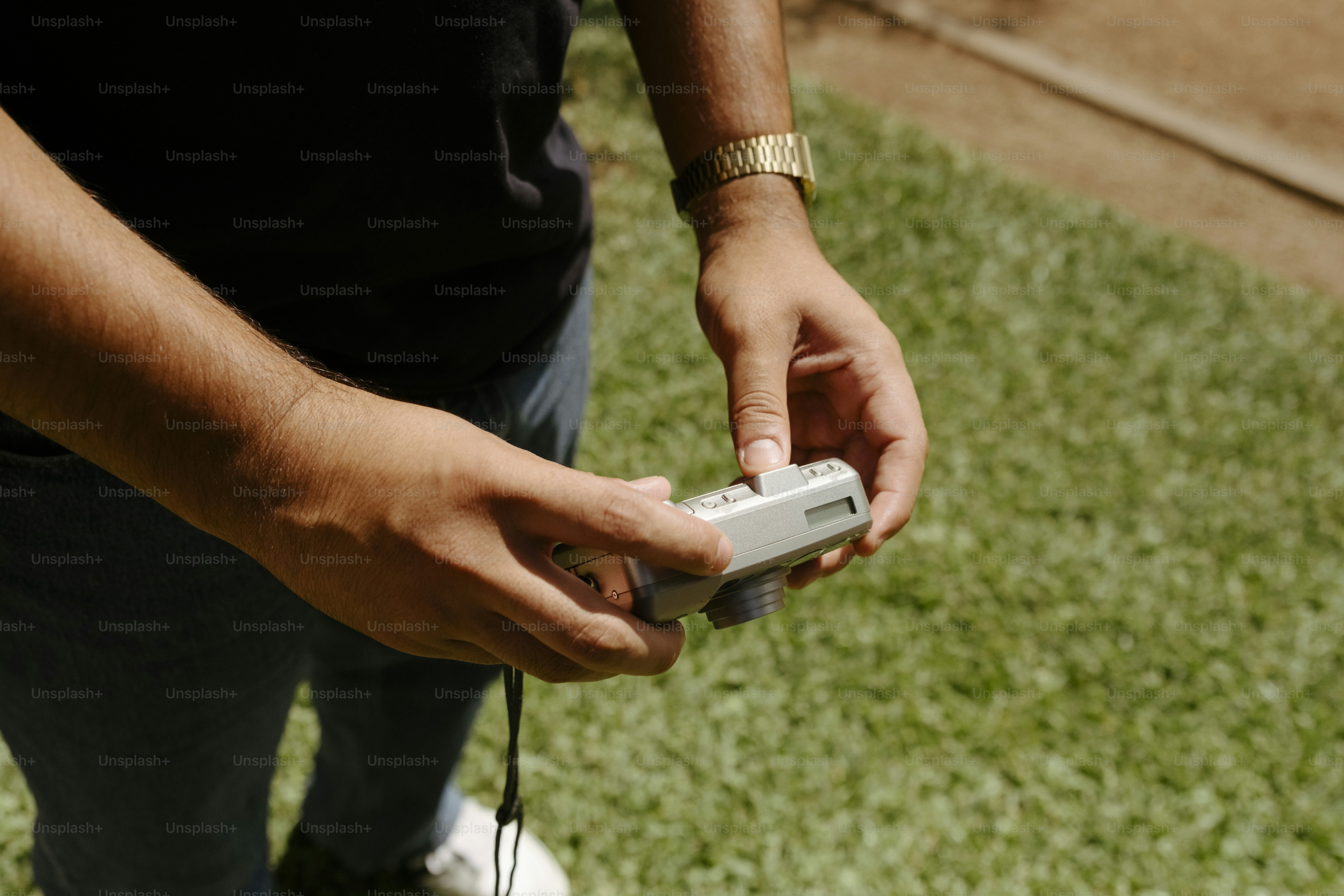 Hands holding a compact digital camera over green grass