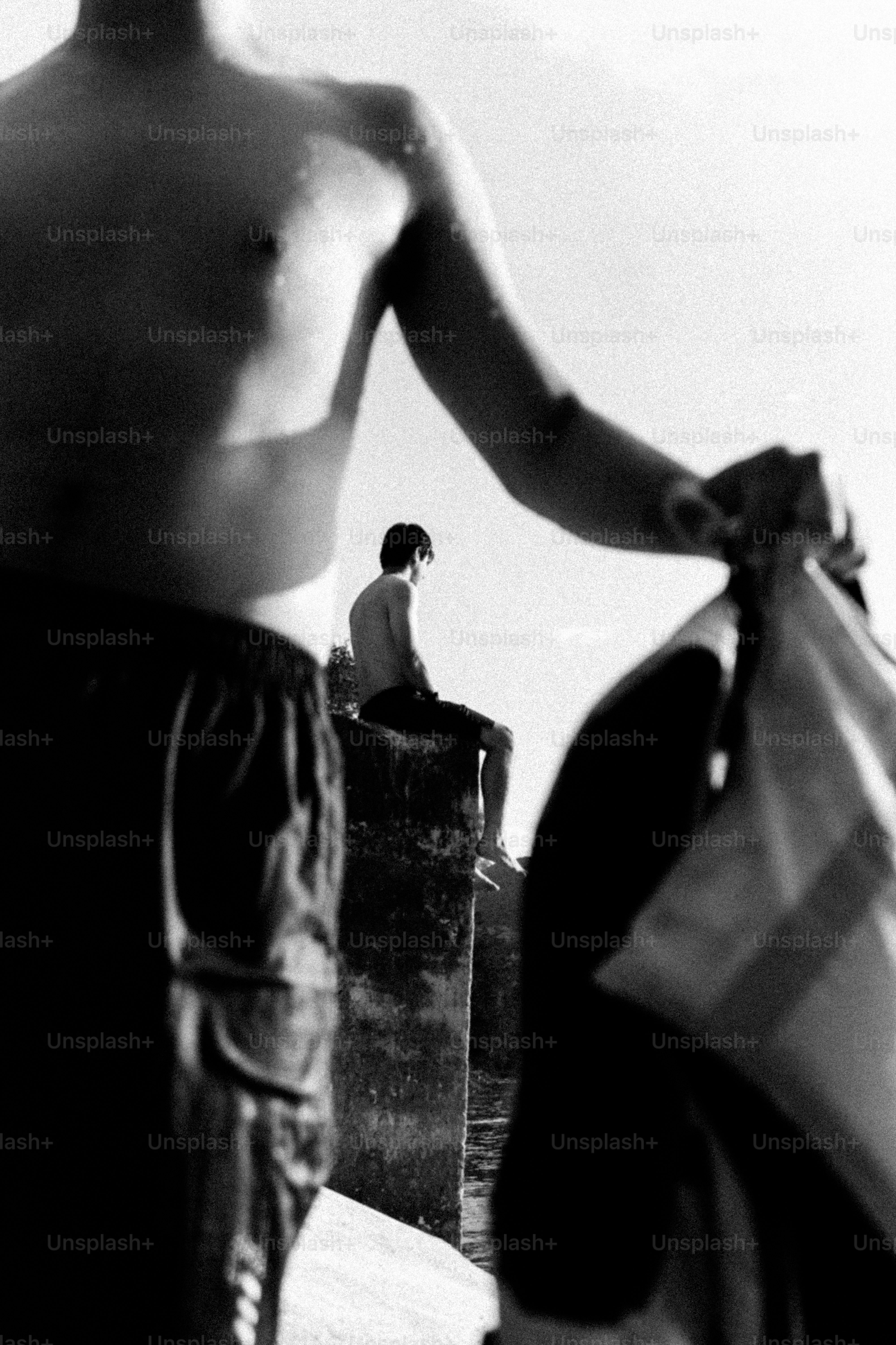 Shirtless man holds clothes, another sits on wall