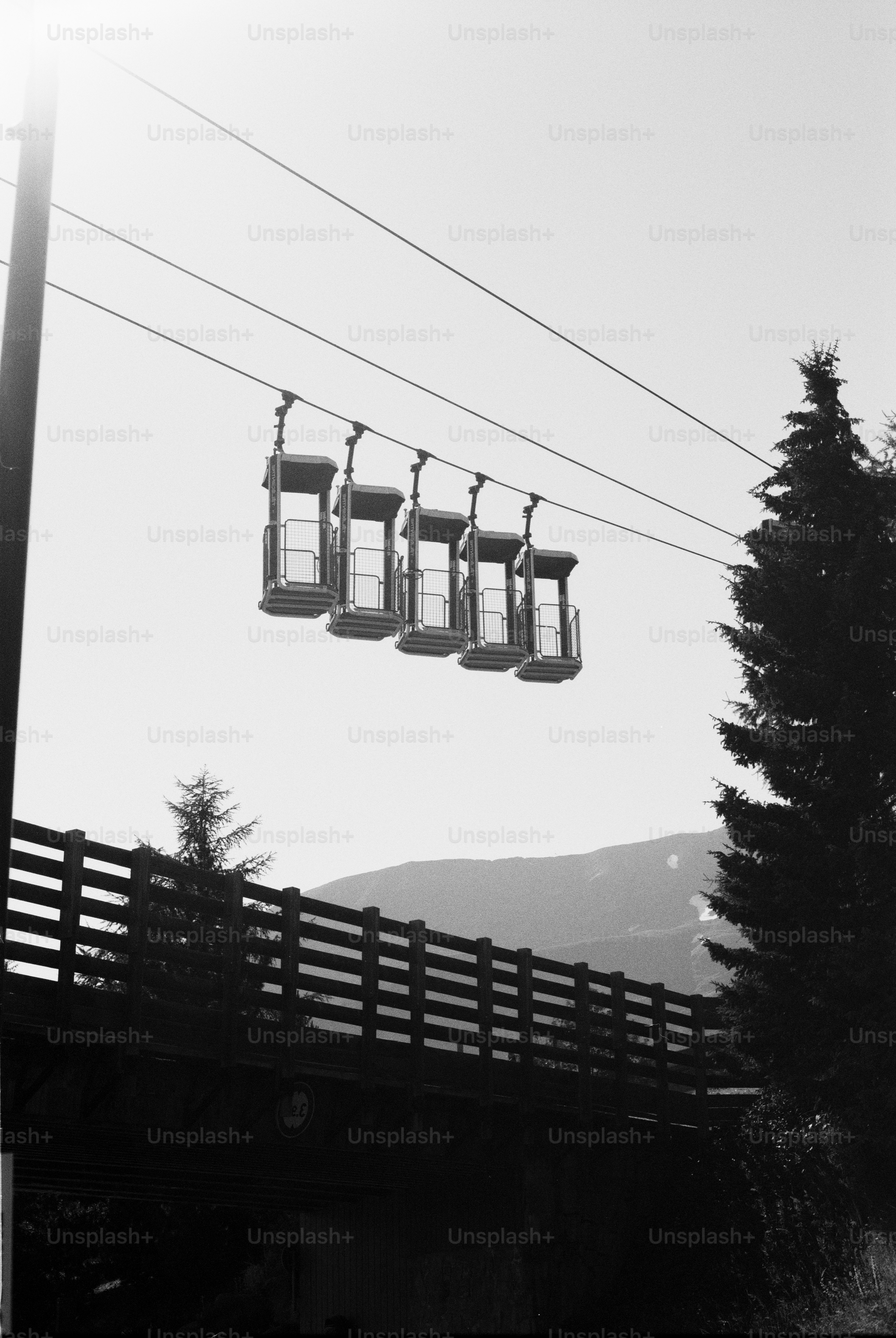 Gondola cabins suspended over wooden fence with mountains
