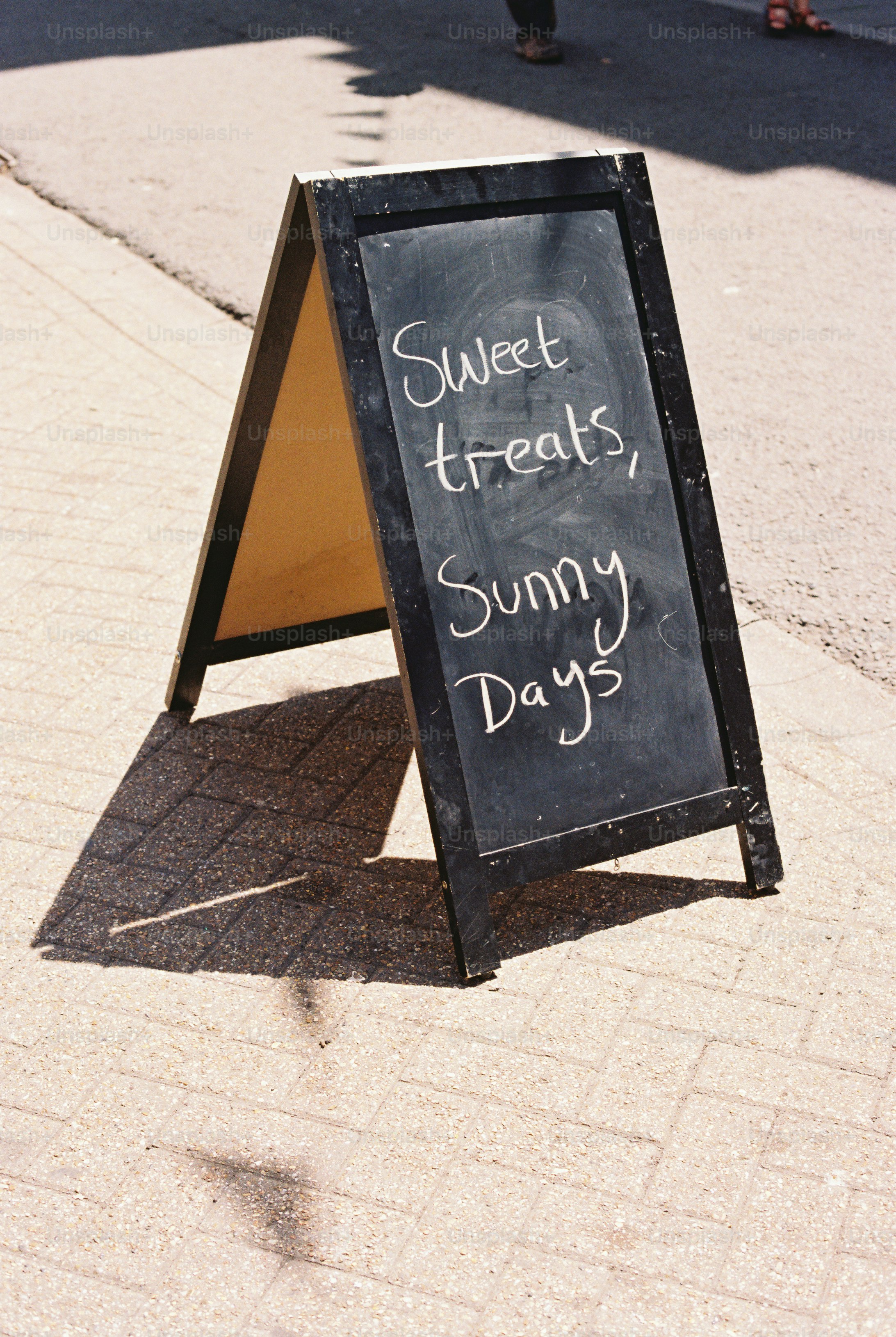 Sidewalk chalkboard sign reading 'sweet treats, sunny days'