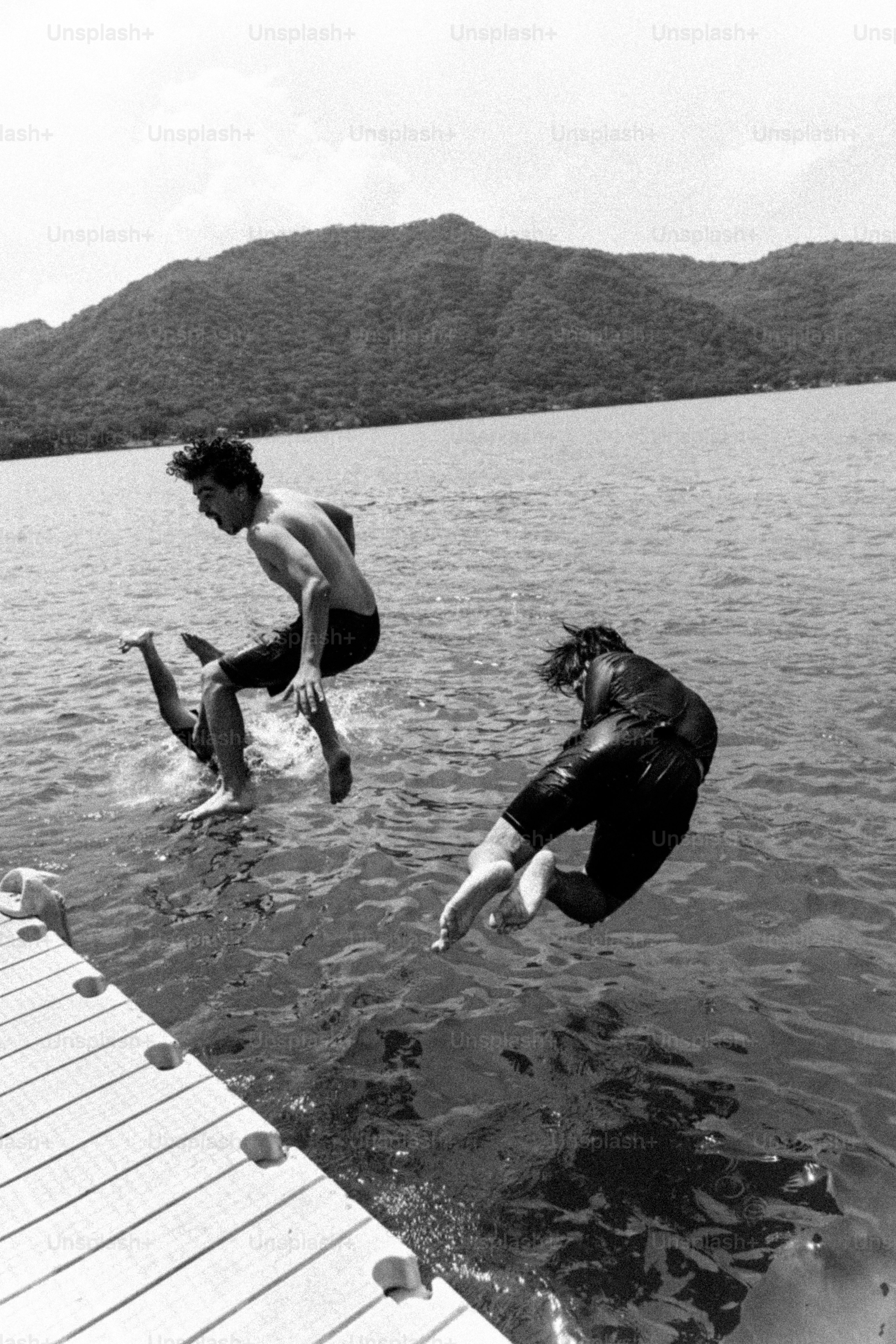 Two people leaping into lake from dock