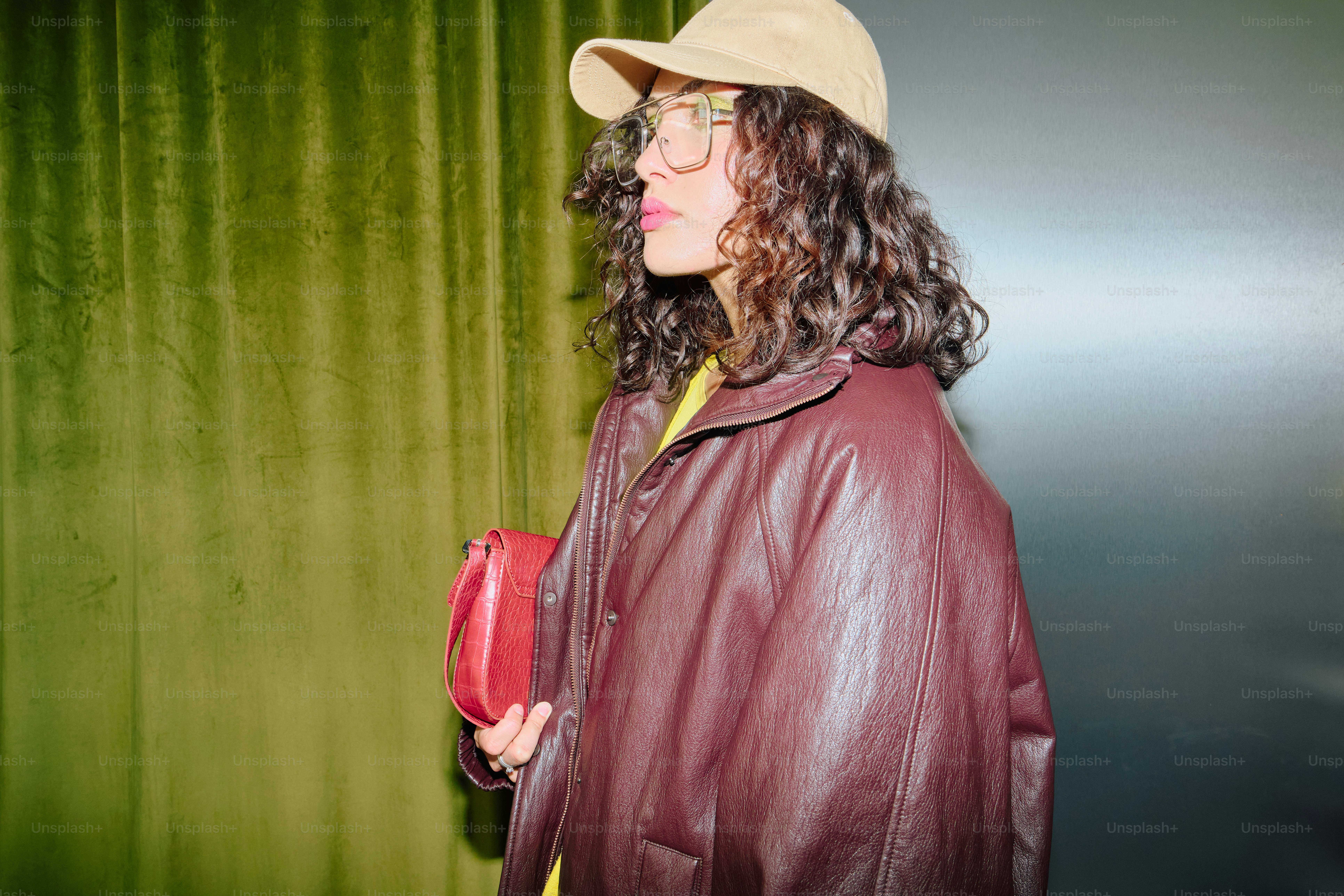 Person in burgundy jacket, beige cap, red clutch