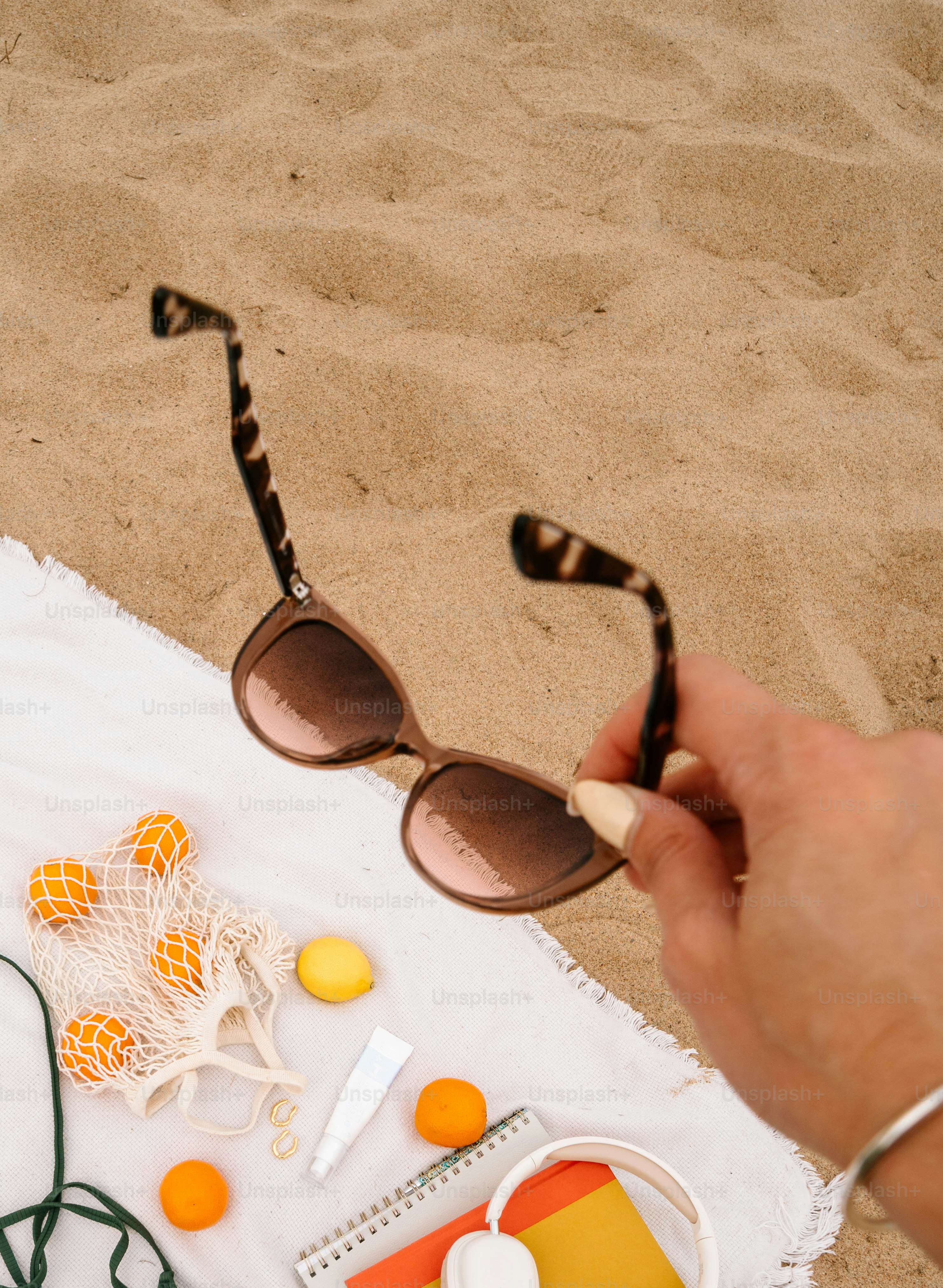 Hand holding sunglasses over beach items on sand