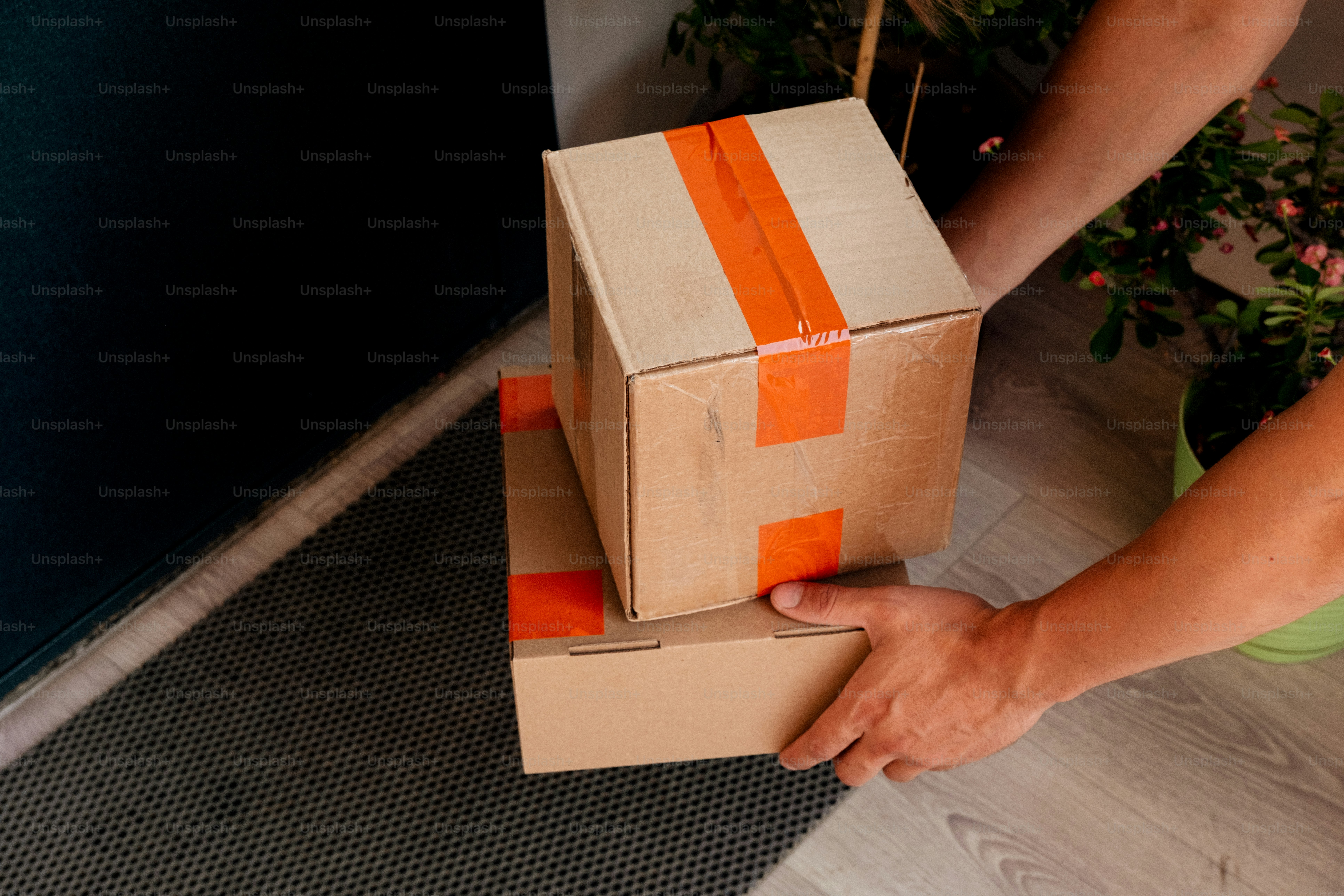 Hands delivering two cardboard boxes to a doorstep